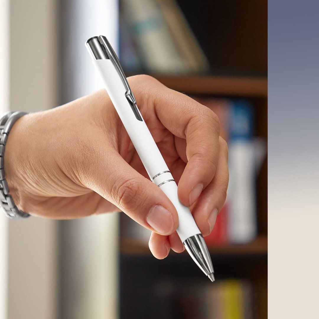 A hand holding a white and silver pen with a bookshelf blurred in the background.