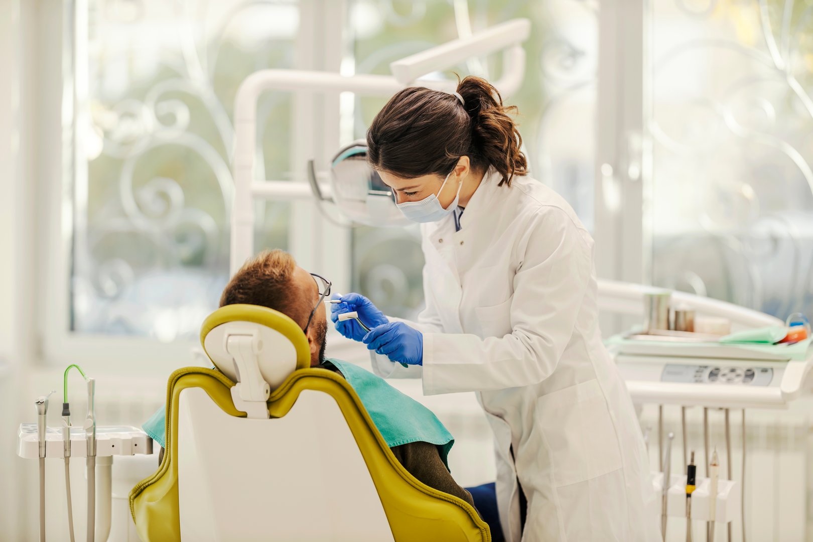 A female dentist is working with patient and fixing bad tooth while standing at dentist office.
