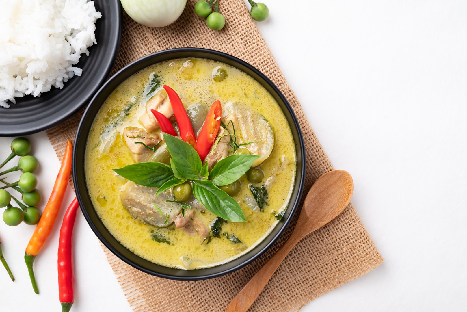 Top view of Thai green curry chicken with rice and ingredients on white background