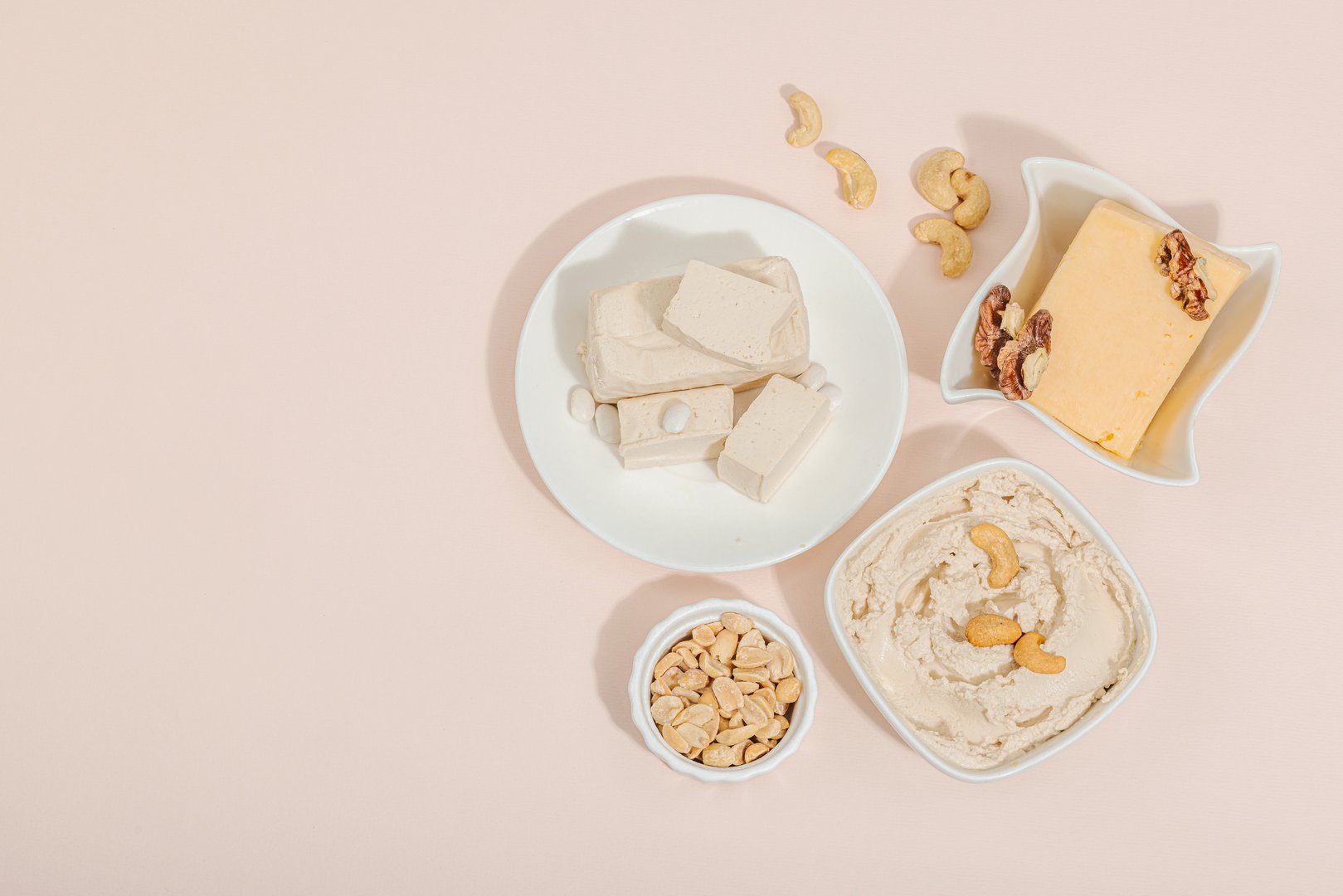 Set of assorted homemade vegan nuts cheese. Raw healthy sauce in a bowl, lactose free food. Bio organic product, plant based diet, alternative lifestyle. Gentle peach background, top view