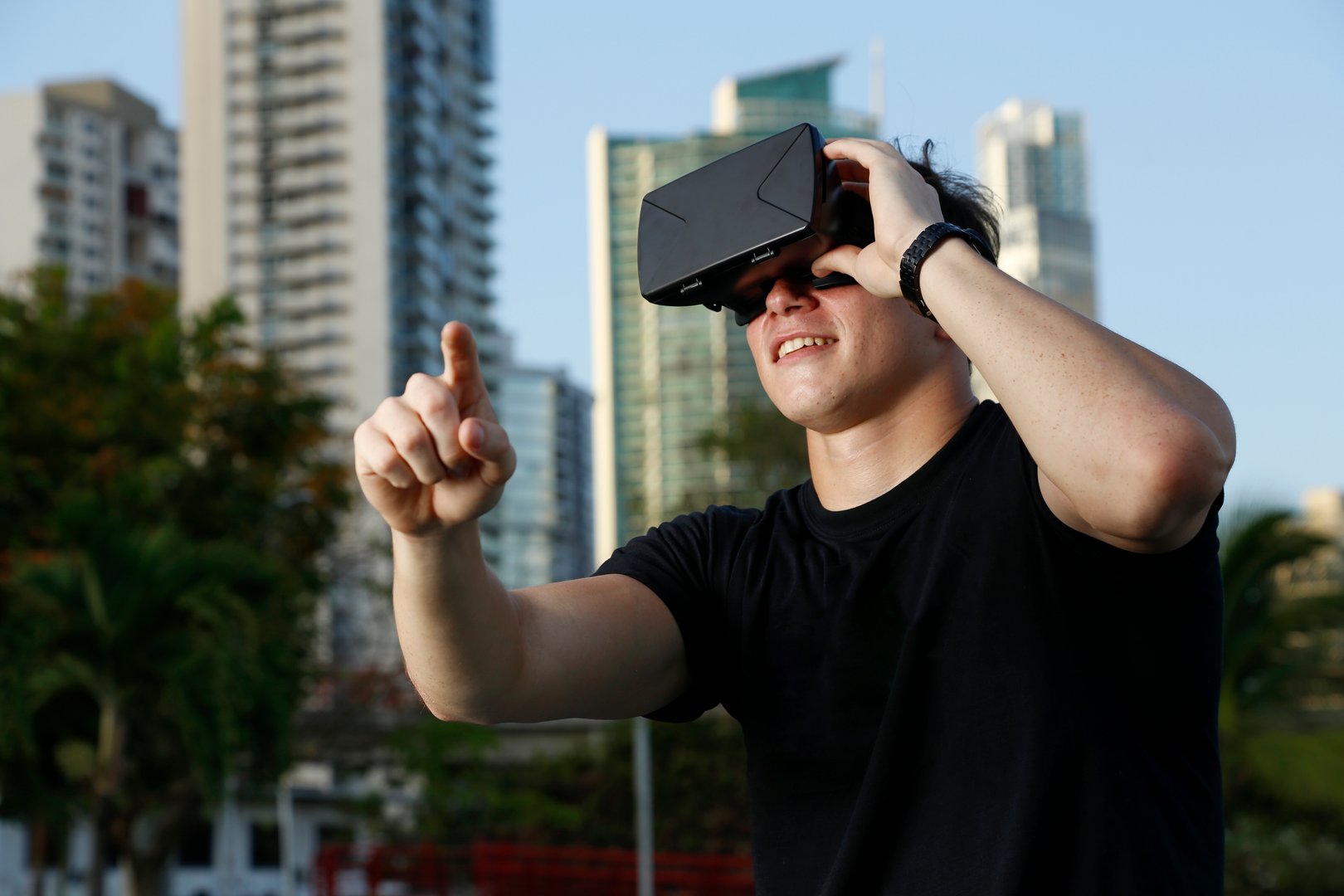 Chico joven con gafas de realidad virtual al aire libre con ciudad de fondo y sueter negro