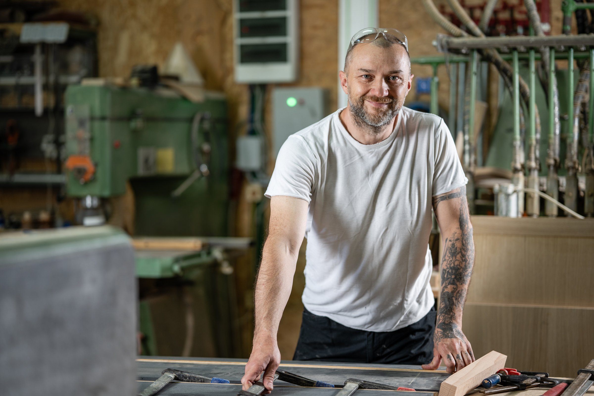 Smiling carpenter working diligently on wood planks in a well-equipped workshop, showcasing skill and craftsmanship in carpentry