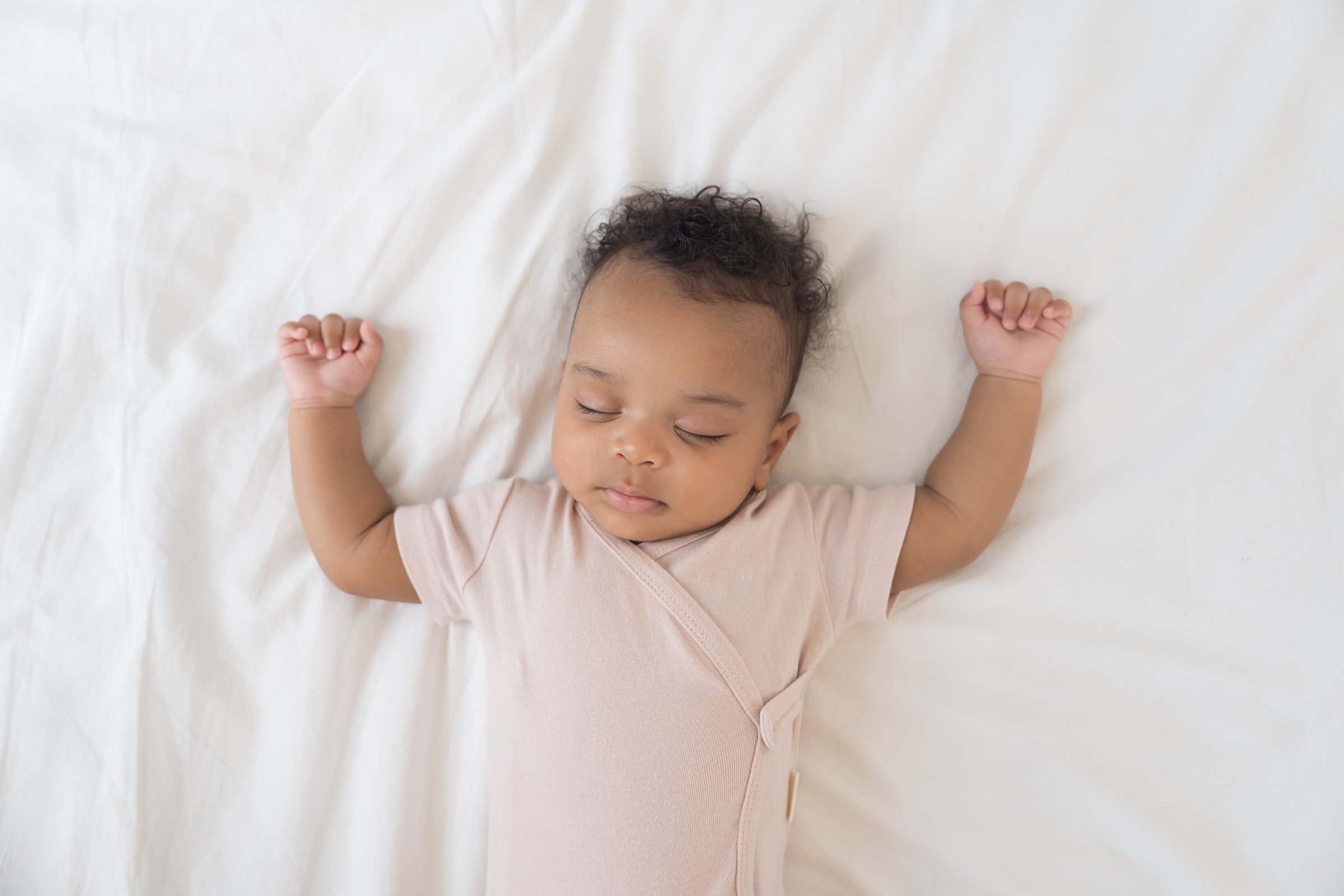 Newborn health care. Top view of newborn baby sleeping on white blanket. African American newborn baby sleeping. Newborn baby in diaper lying on bed