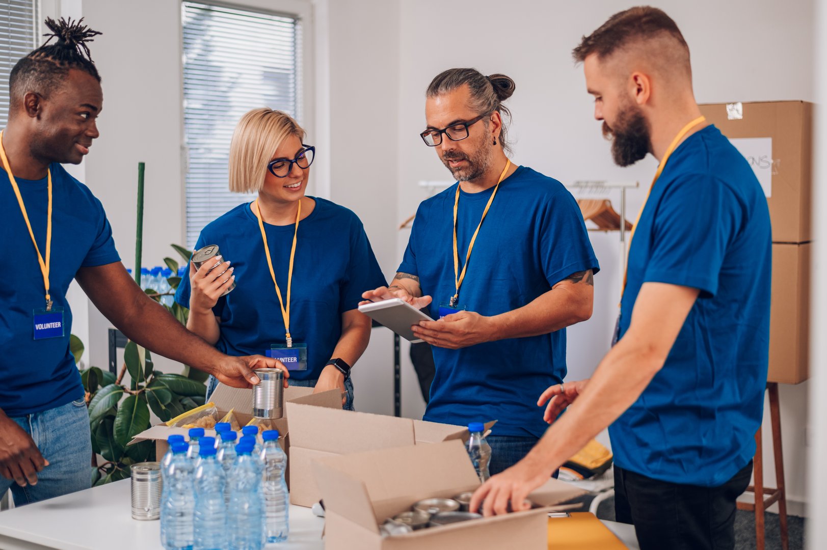Multiracial volunteers working in community charity donation center and using a tablet while wearing blue t shirts. Diverse volunteers collecting food donations in a warehouse. Copy space.