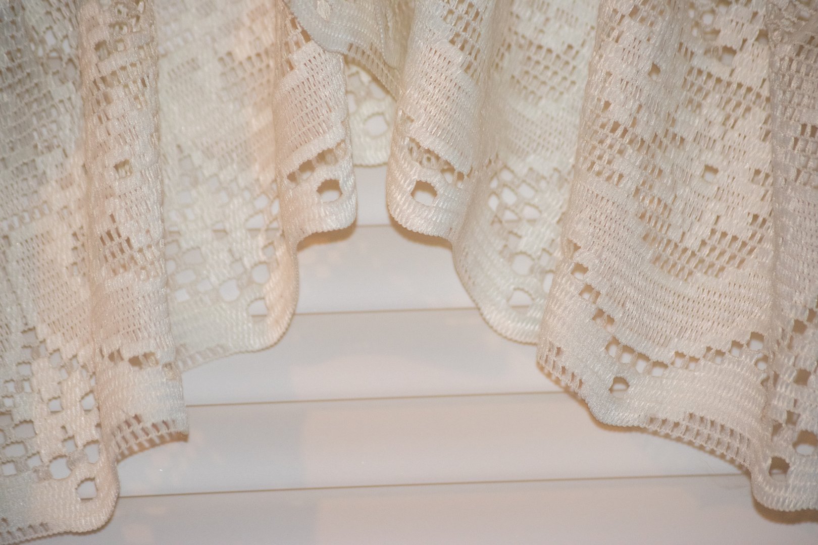 Detailed image of an intricate white lace fabric showcasing elegant patterns and textures. The delicate design highlights craftsmanship, adding a touch of elegance and vintage charm.