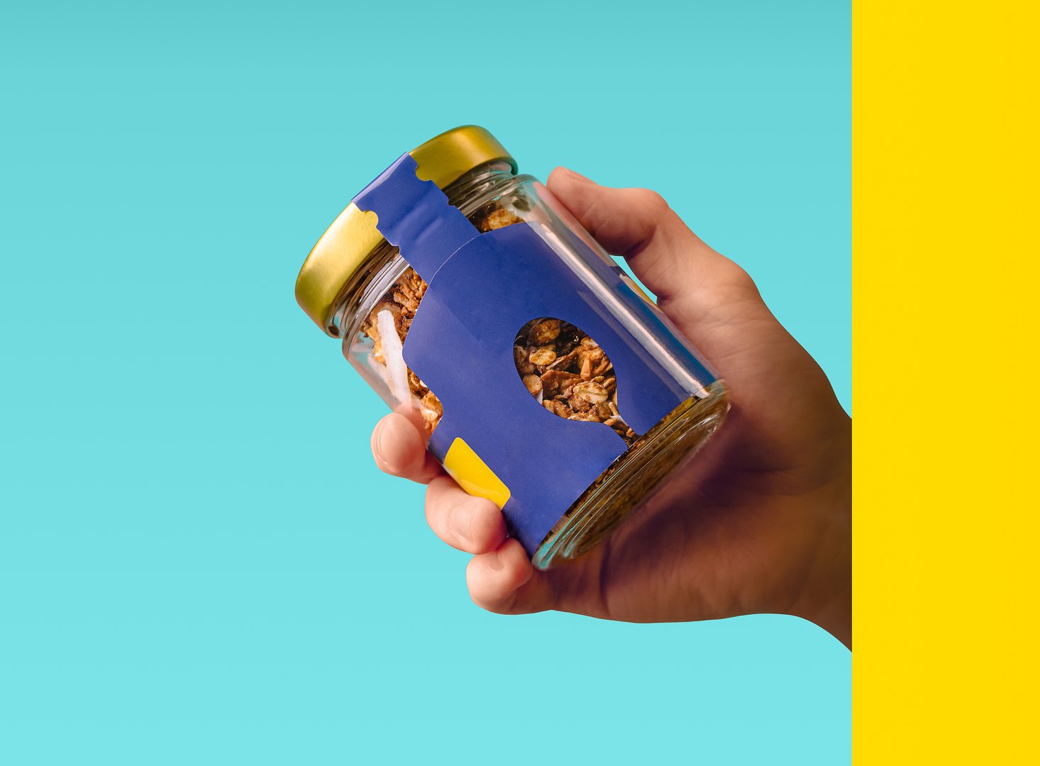 A hand holds a uniquely designed snack jar with colorful packaging. The jar contains granola, set against a turquoise background that highlights its modern aesthetic.