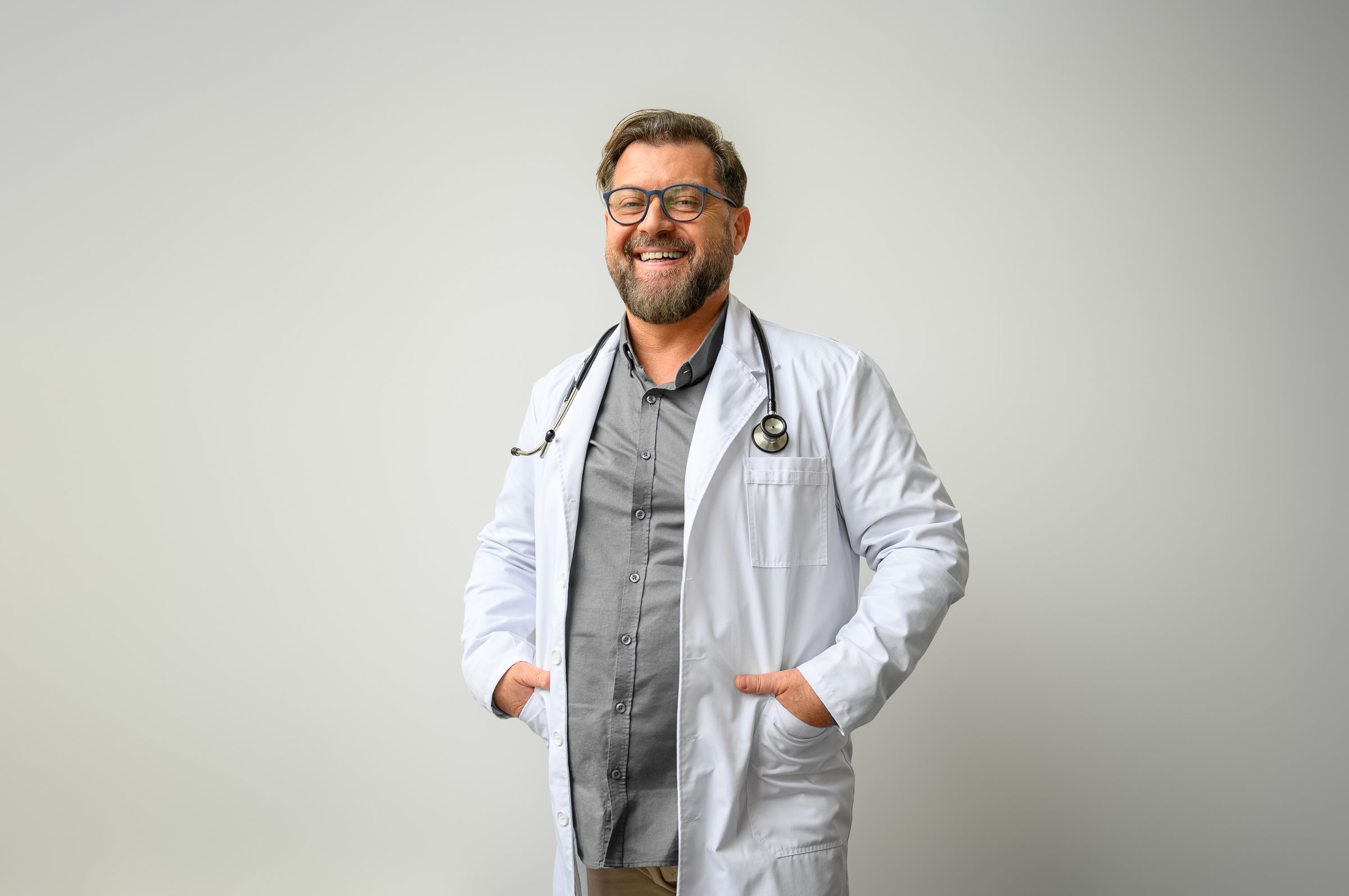 Portrait of male medical professional in lab coat with hands in pockets standing on white background