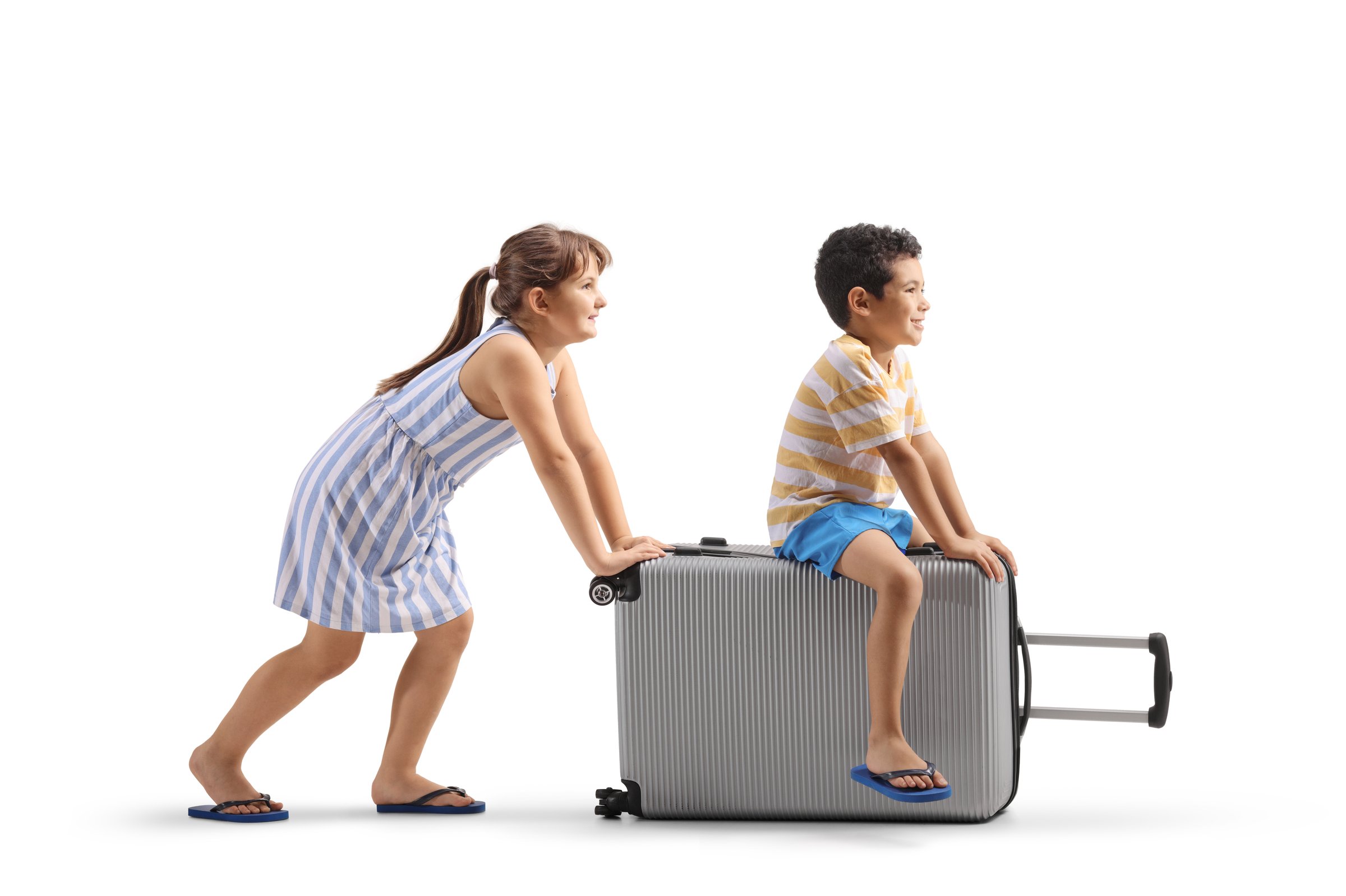 Girl pushing a boy seated on a suitcase isolated on white background
