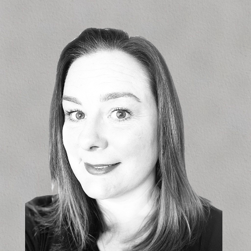 Woman with shoulder-length dark hair wearing a light-colored top against a blurred background.