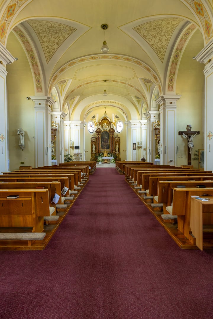 Church interior featuring rows of empty wooden pews leading to a decorated altar
