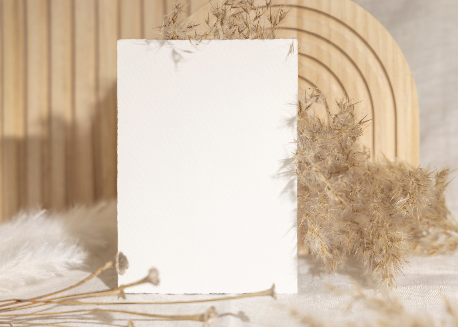 Blank card near dry pampas grass and beige wooden decor on linen closeup, minimal mockup. Boho scene with vertical card, Bohemian or close to nature wedding stationery or party design