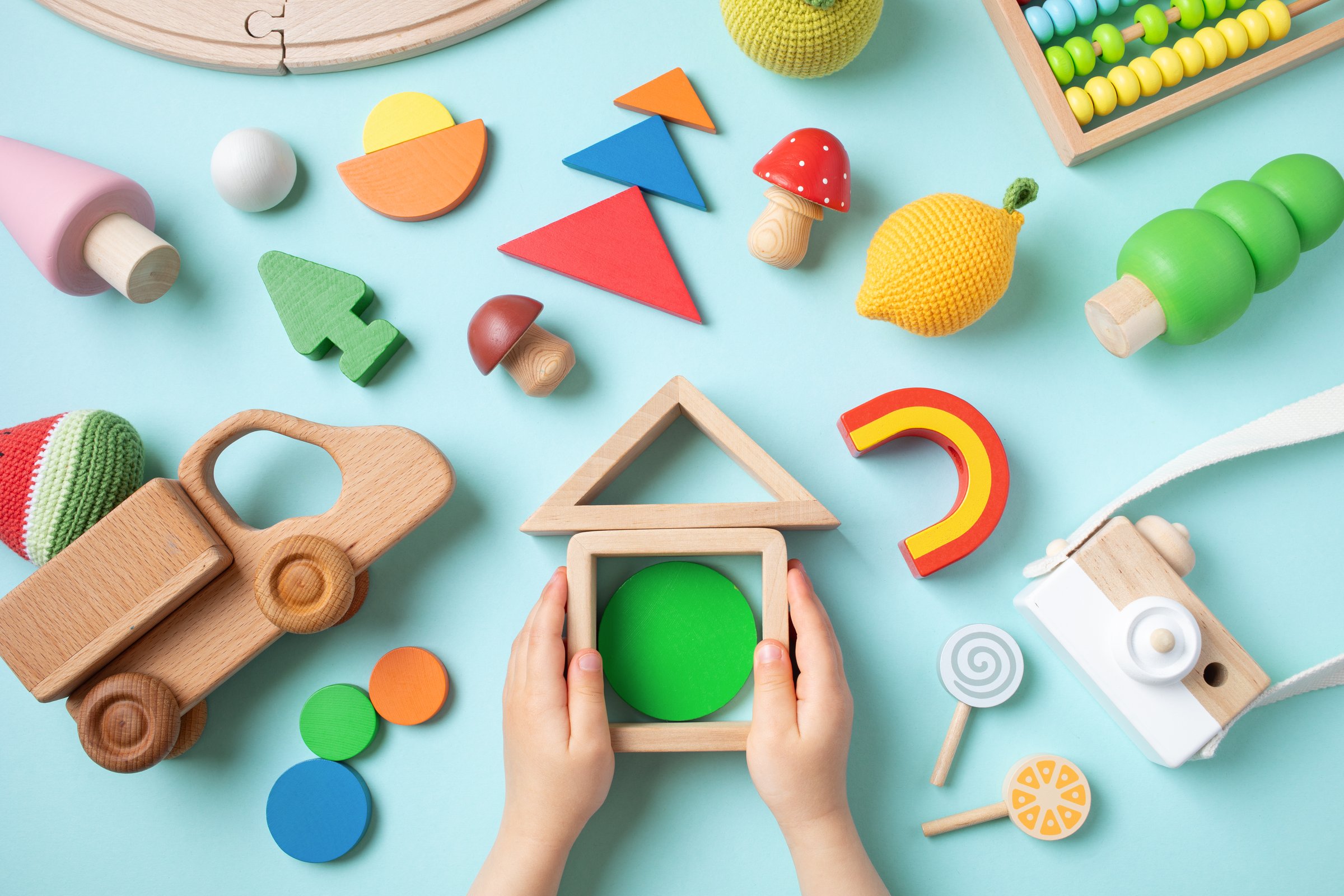 Toddler children activity for motor and sensory development. Baby hands with colorful wooden eco toys on table from above.