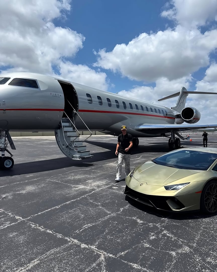 Man standing on tarmac near a private jet and a gold Lamborghini, with blue sky and clouds in the background.