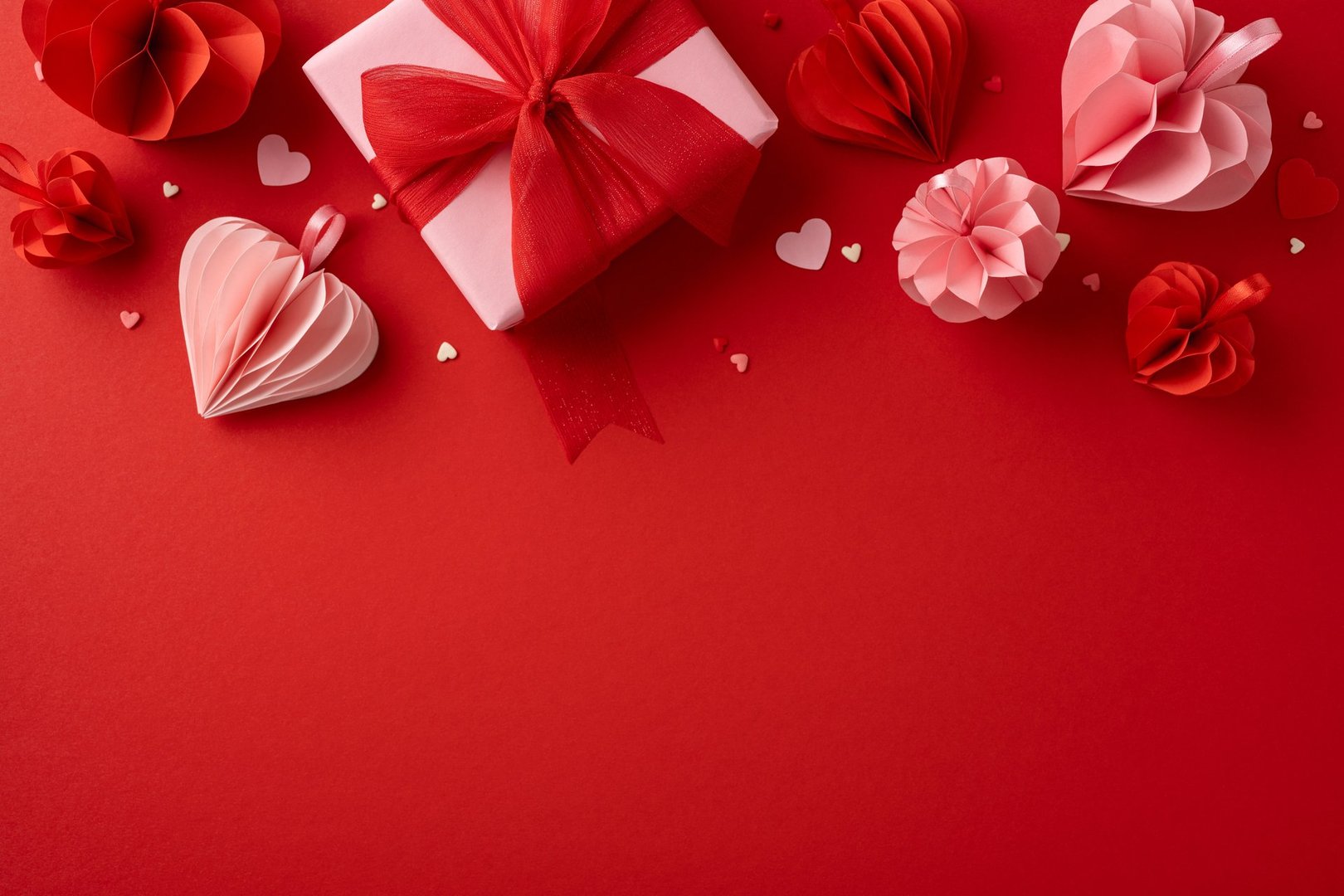 A beautifully wrapped gift box on a red background, surrounded by paper hearts and decorations, creating a romantic Valentine's Day atmosphere