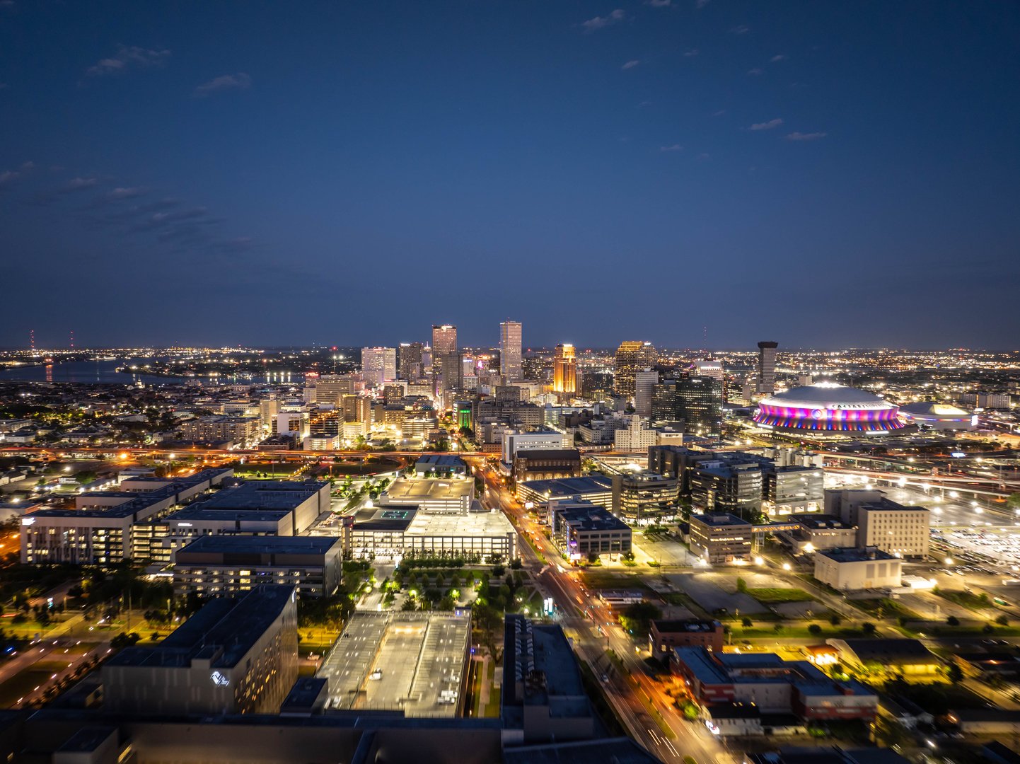 Glowing New Orleans city skyline at dusk with illuminated buildings, busy streets, and the Caesars Superdome, creating a captivating urban night view.
