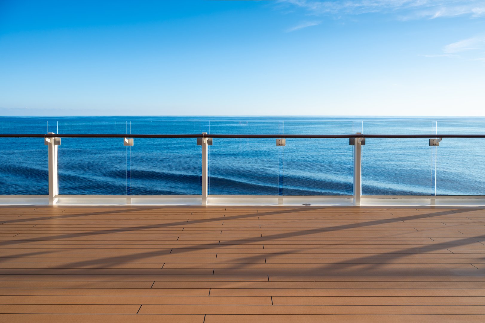 Luxury wooden cruise ship deck with safety railing, blue sky and calm sea on a beautiful summer vacation day.