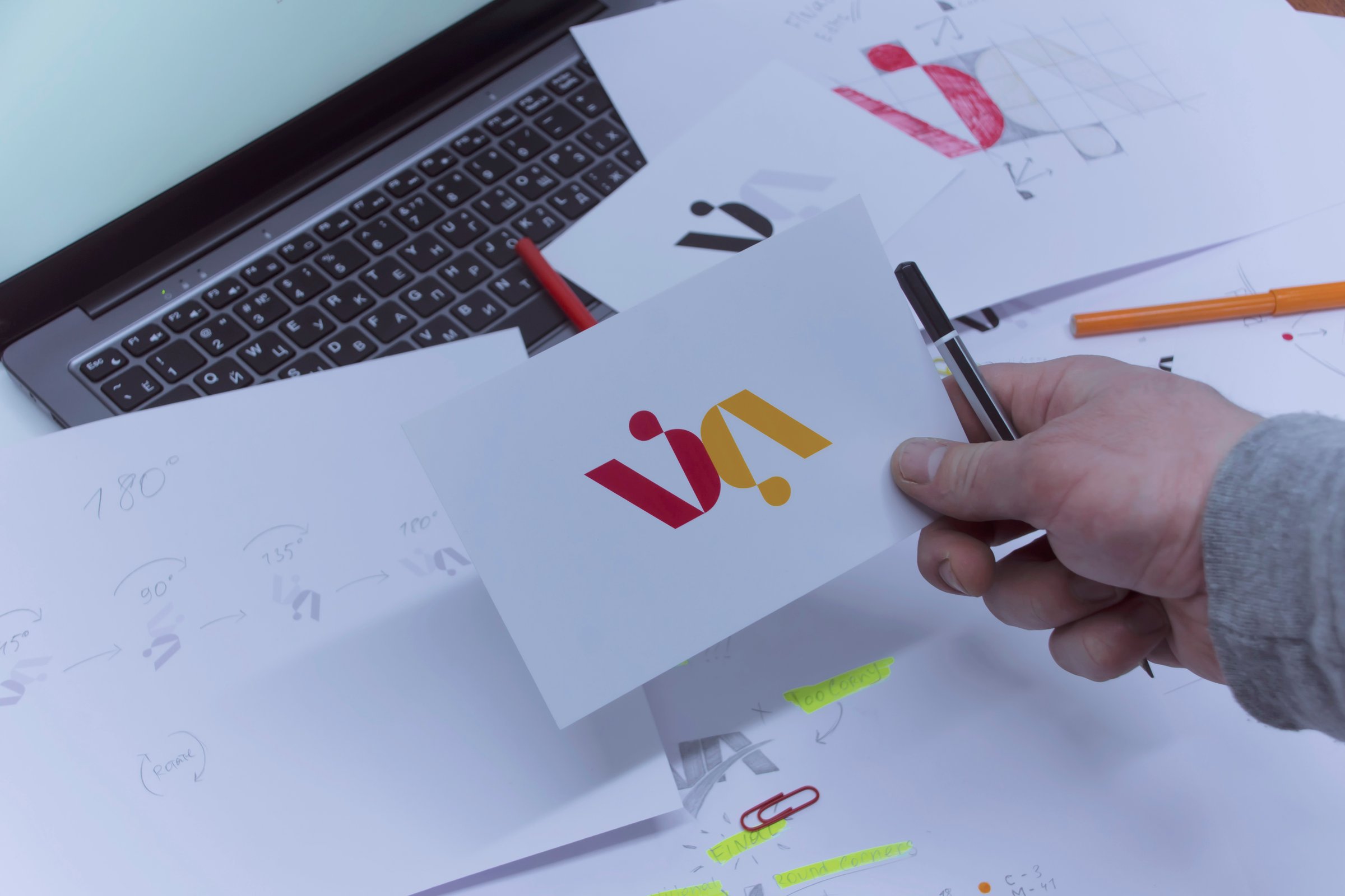 Creative workplace of a Graphic Designer. A man in the office is developing a logo on the table against the background of printed sketches and a laptop
