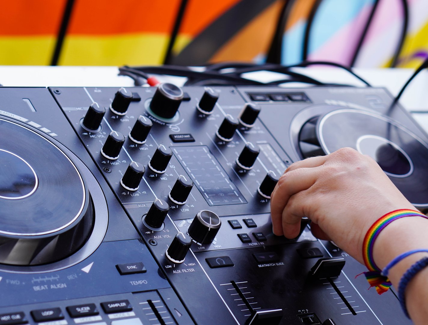 Dj on mixing desk with rainbow bracelet and flag . playing music at gay pride party.