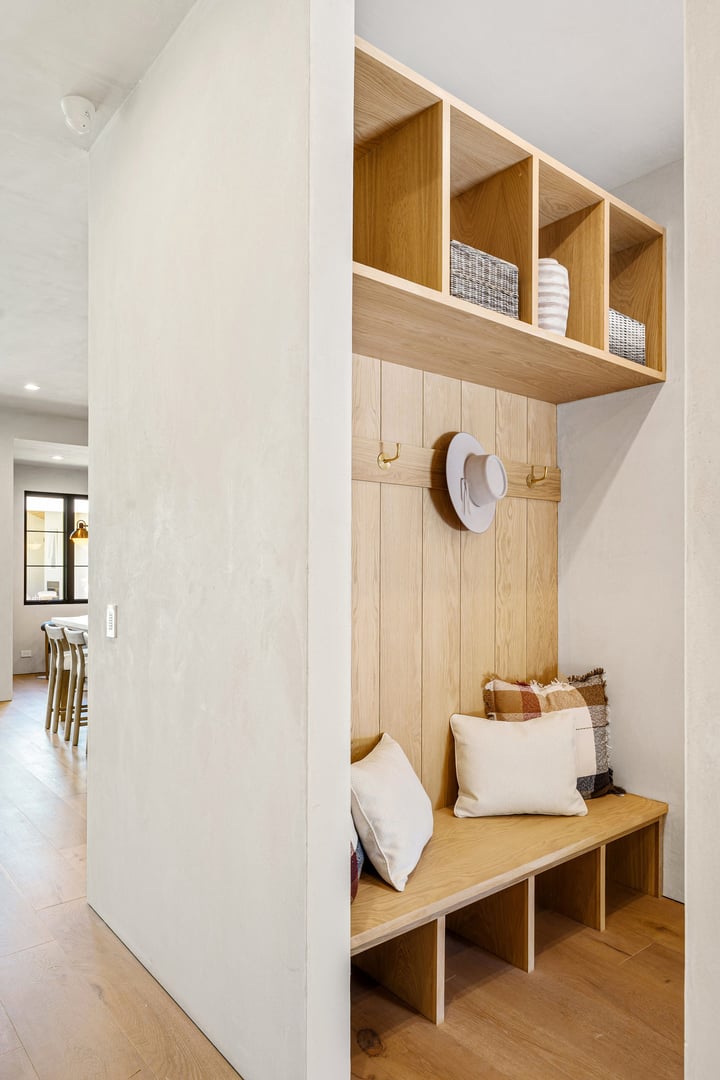 Modern entryway with wooden bench, pillows, and storage shelves in a bright home interior.