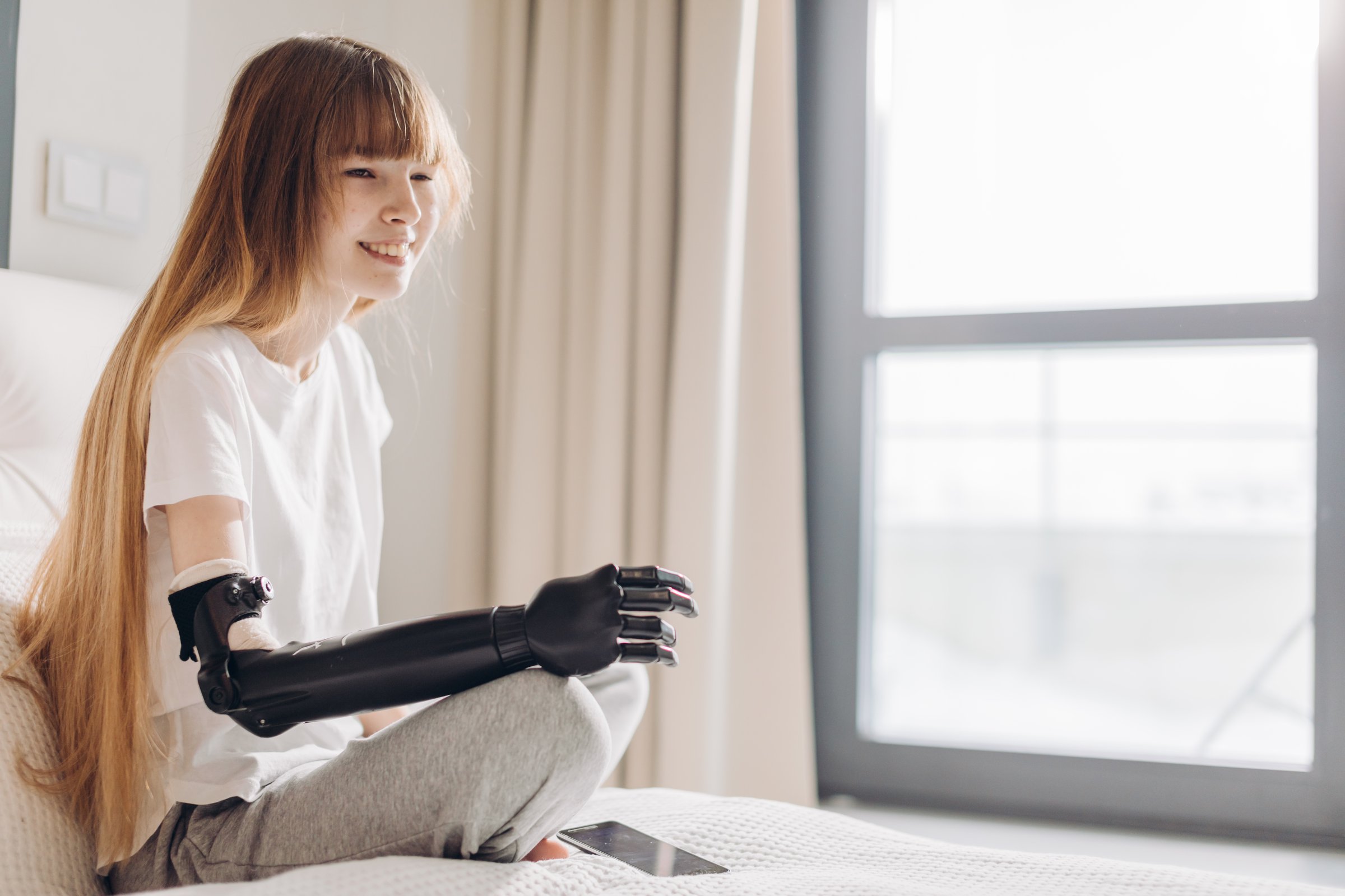 pale cheerful girl wearing a cyber hand sitting near the window in the clinic. copy space.innovation. the willingness to live