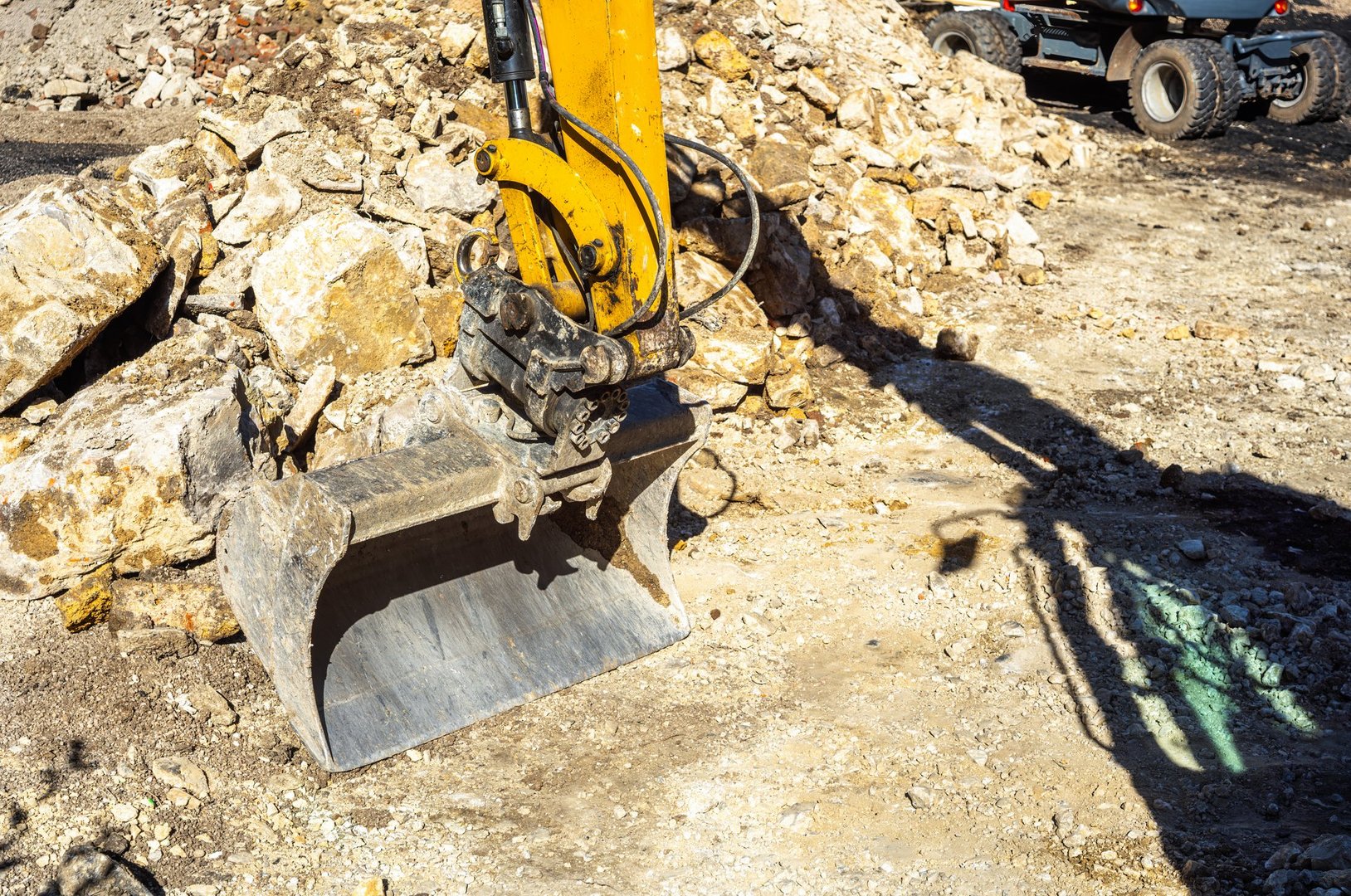 A close-up of an excavator bucket on a construction site, surrounded by rocks and gravel, showcasing heavy machinery in action