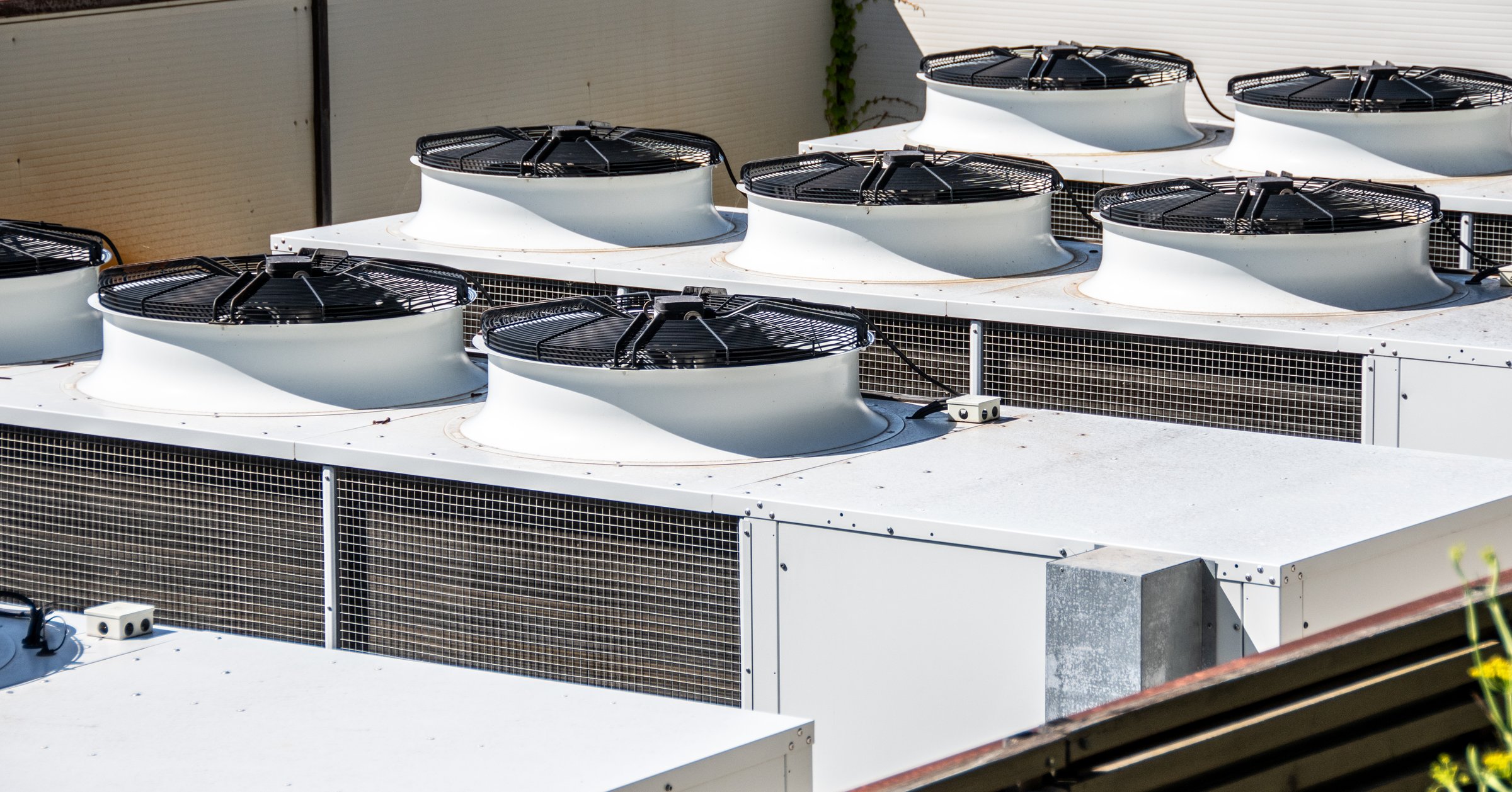 Multiple industrial air conditioning units installed on a commercial building's roof, showcasing urban infrastructure and modern HVAC technology. White and black cooling units, highlighting functionality and design in commercial settings.