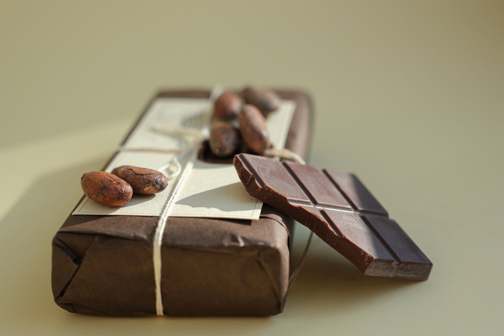 Package of Chocolate Bars in Eco-Friendly Packaging, Soft Sunlight. Bitten Piece of Chocolate. Cocoa Beans. Brown and Beige Shades. Chocolate Gift Concept. Shallow Depth of Field.