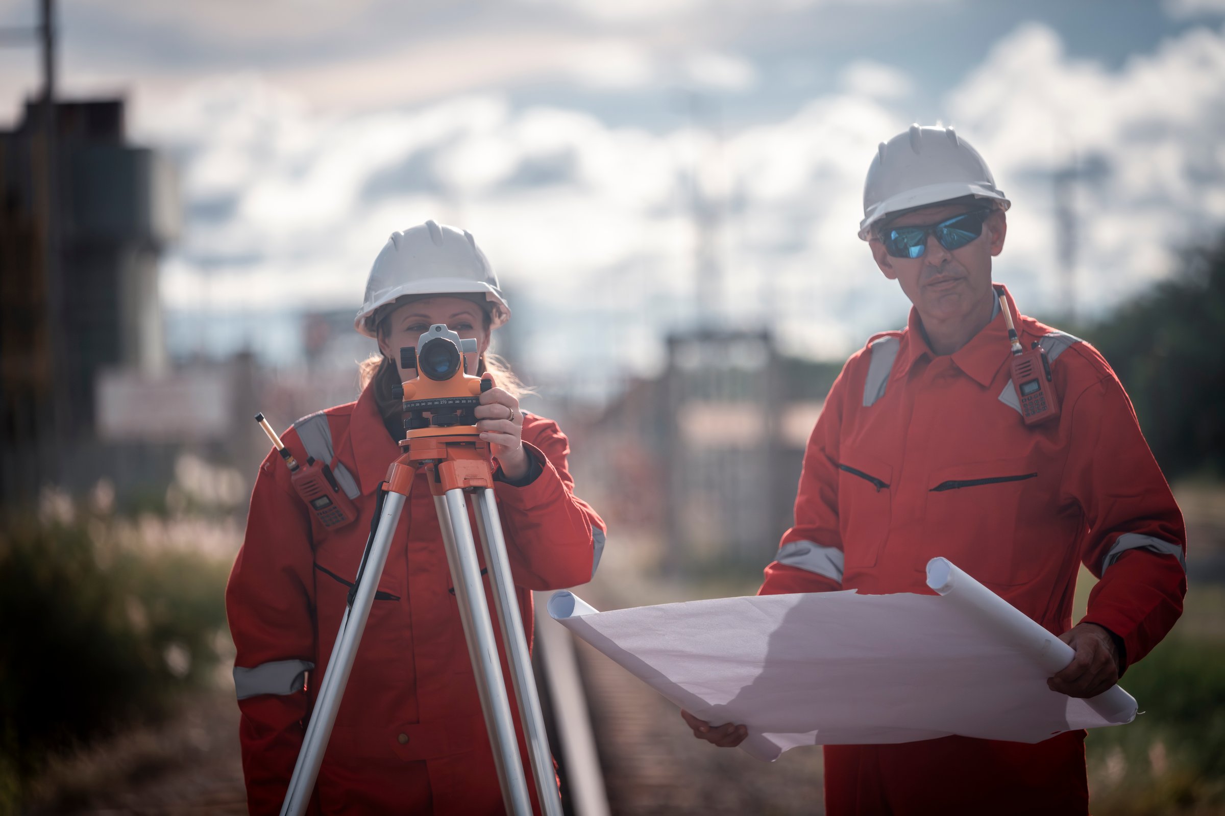 Surveyor engineers team wearing safety uniform and blueprint checking inspection by theodolite telescope to measurement level position railway construction site is industry transportation concept.