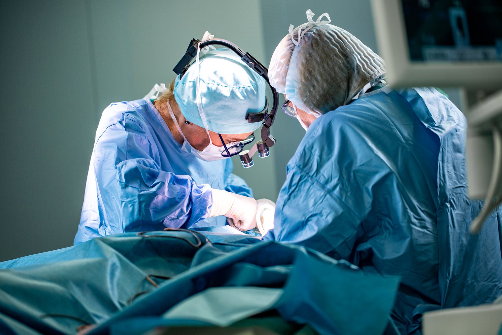 Surgeon and his assistant performing cosmetic surgery in hospital operating room. Surgeon in mask wearing loupes during medical procadure. Breast augmentation, enlargement, enhancement
