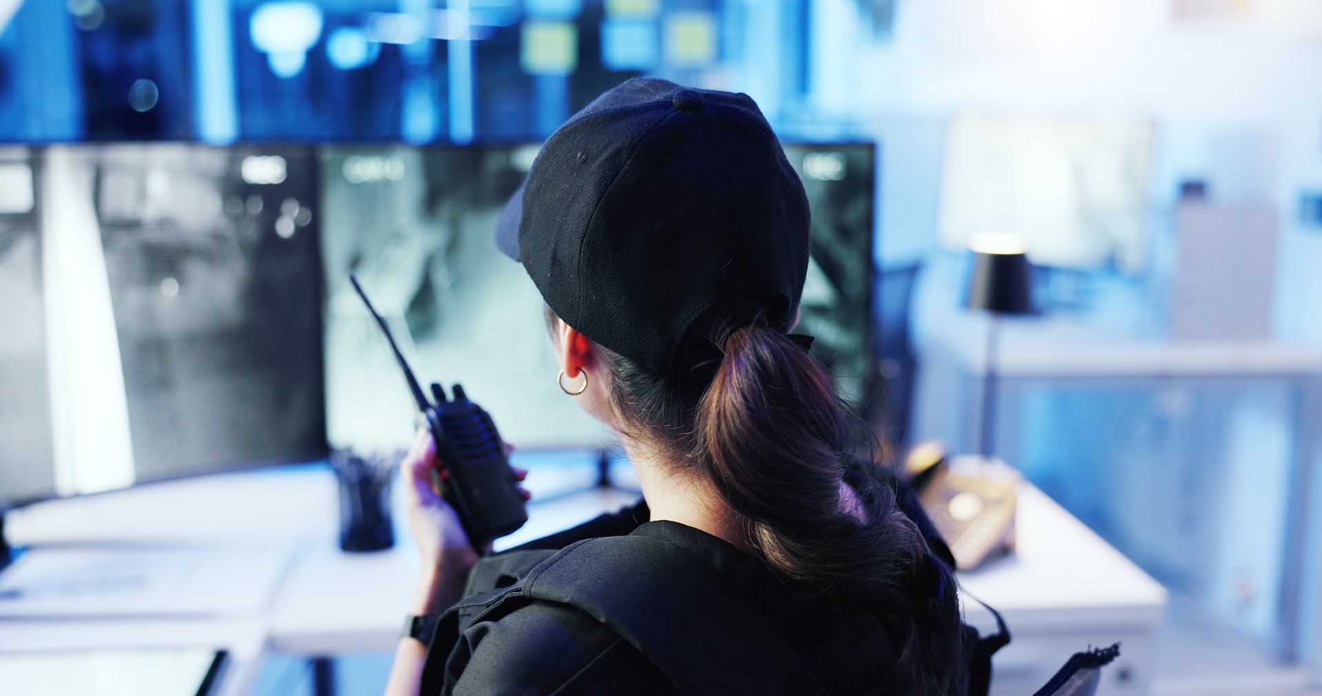 Control room, surveillance and woman with radio, watching and back of security guard, night or footage. Observation, camera and person with tech for communication, law enforcement or safety with cctv