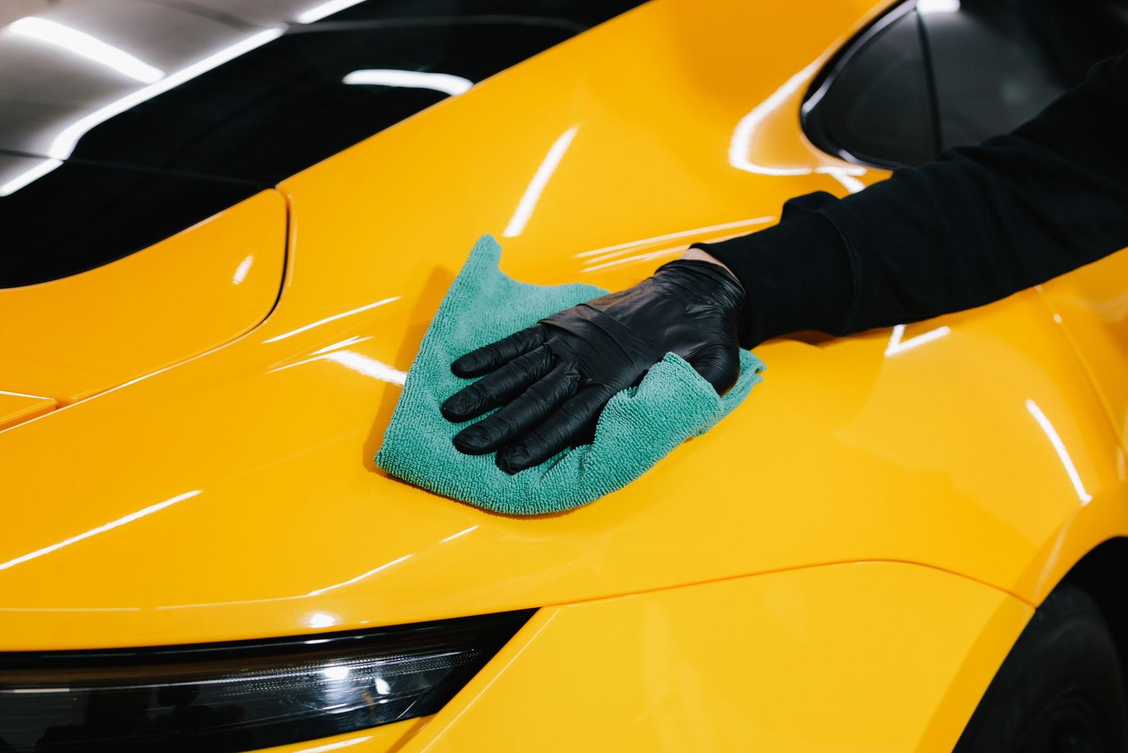Manual washing and polishing car with microfiber cloth after detailing procedure. Microfiber hand cleaning and washing sports car using microfiber towel in garage