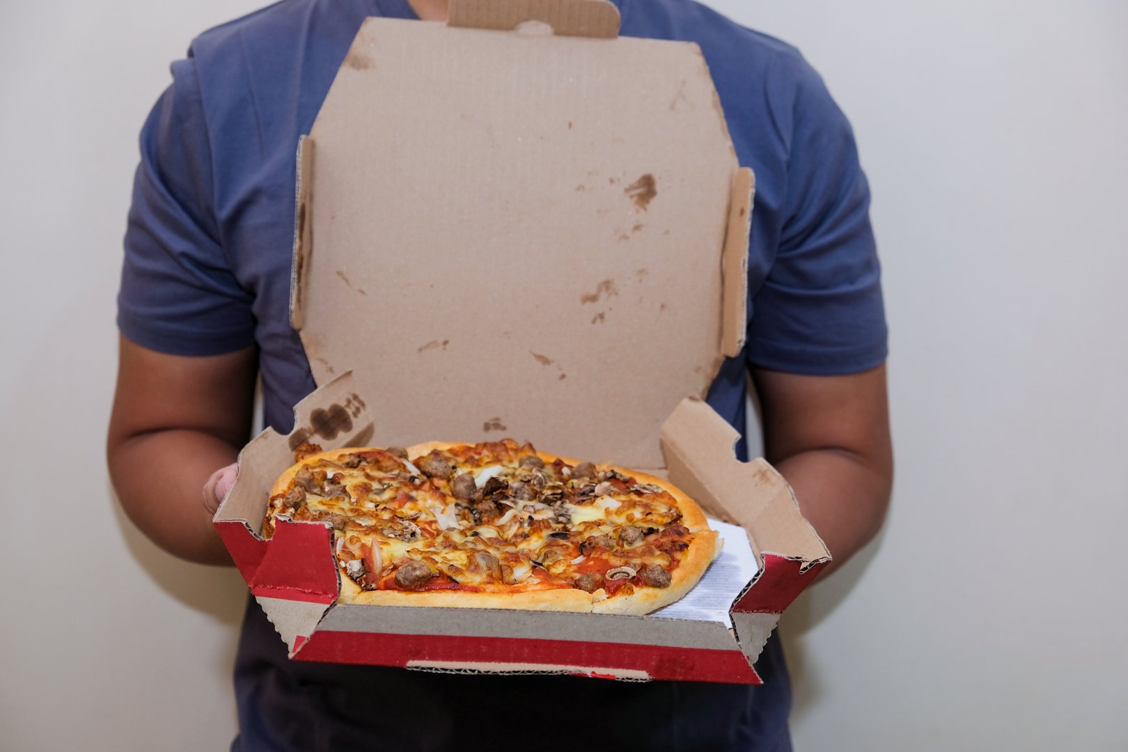 Closeup of a man hand holding box with pizza,  cream isolated background, showing fast food