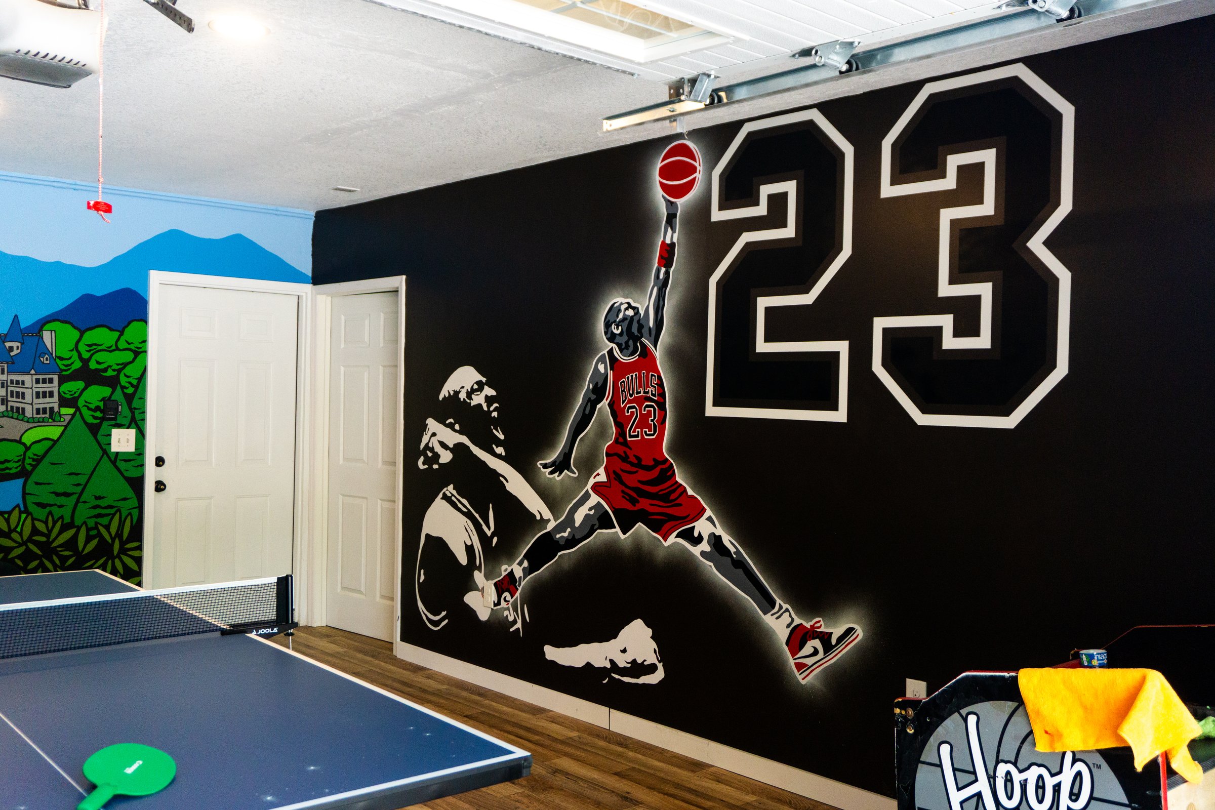 Room with a table tennis setup and a large mural featuring a basketball player silhouette and the number 23 on the wall.
