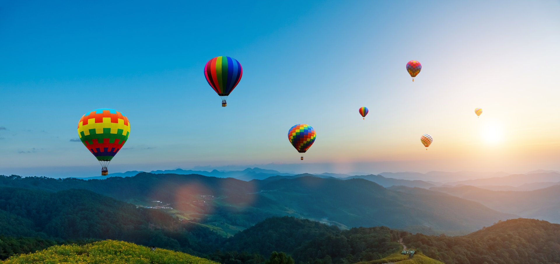 Colorful hot air balloons flying over mountain at sunset sky background