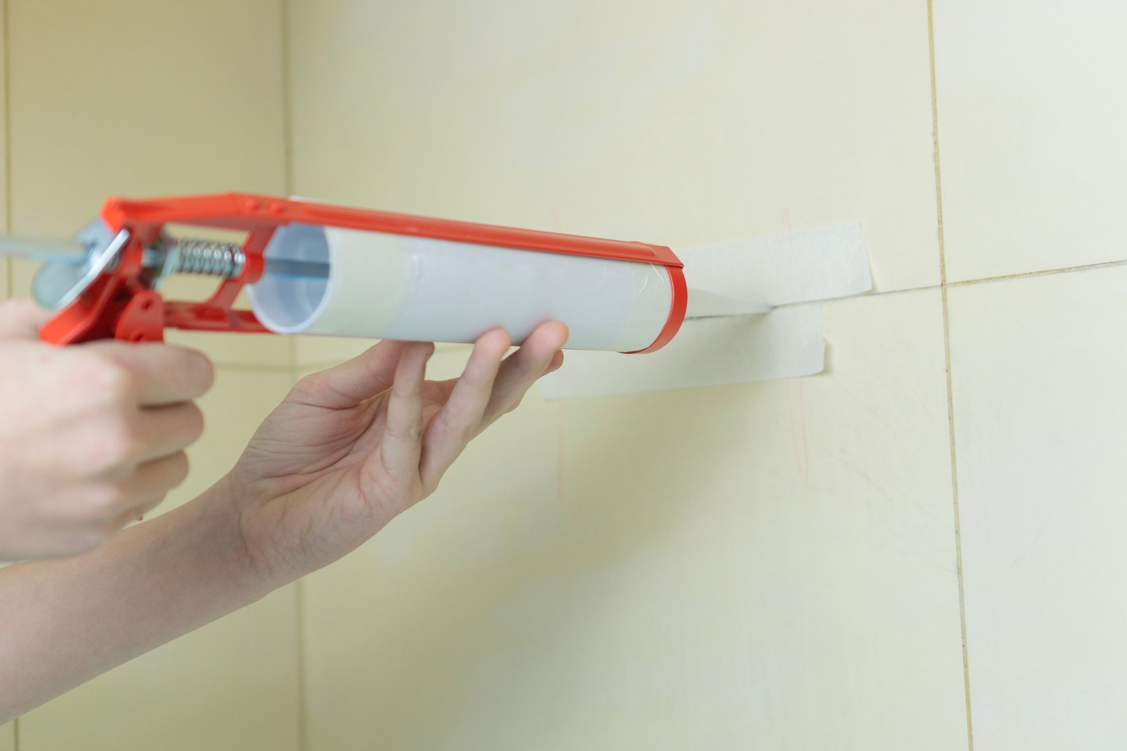 Hands applying silicone sealant on tile joints