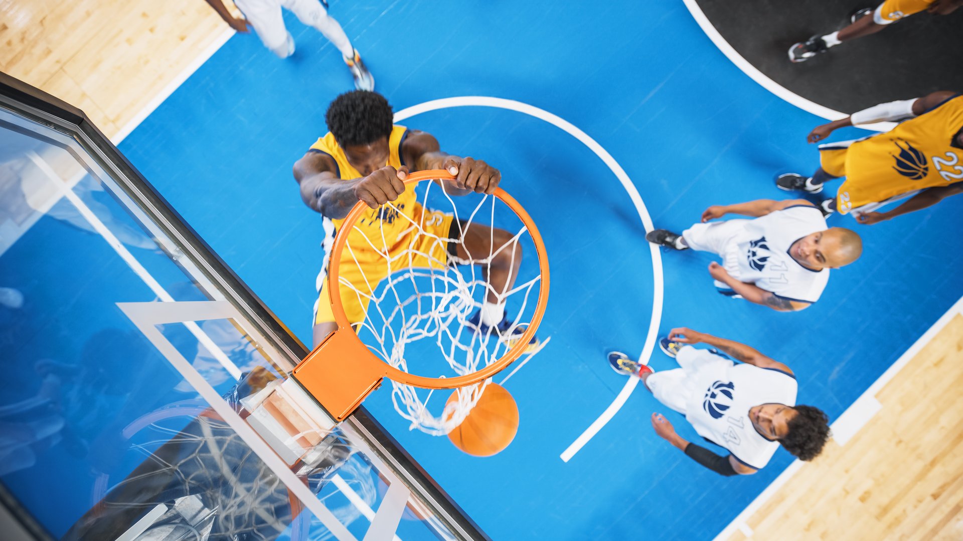Cinematic Shot of Basketball Action for Live TV Channel: Top Down Photo of an African Yellow Team Player Scores a Powerful Slam Dunk Goal and Hangs on the Hoop To Celebrate Successfully Achieved Point
