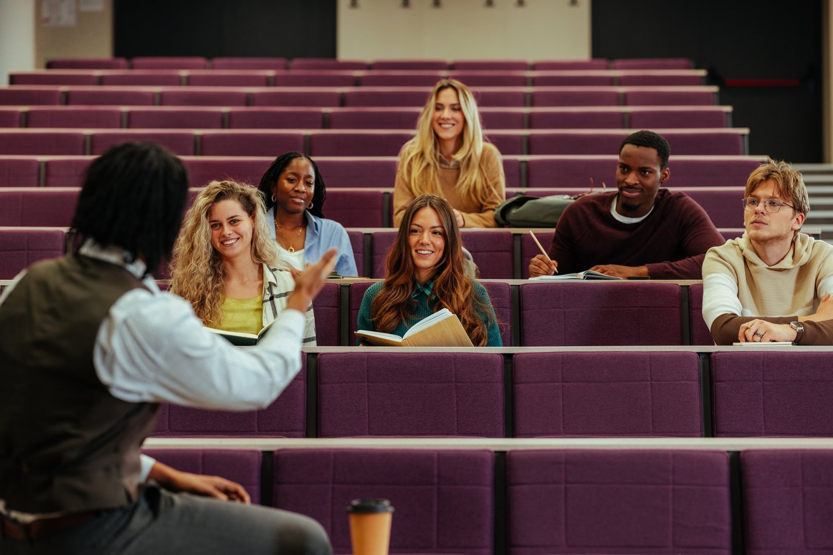 University professor gesturing while interacting with diverse group of attentive students in a lecture hall