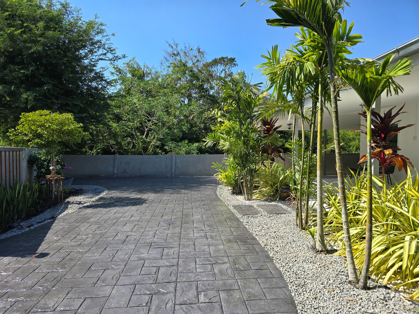 A beautifully crafted stamped concrete pathway leads through vibrant plants in Pattaya, Thailand. a Thai Suburban area with a modern family house