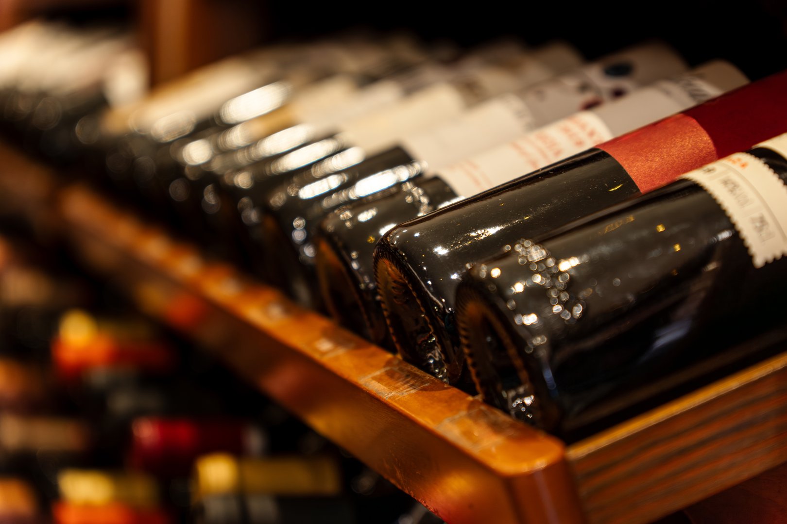 Close-up detail of several black red wine bottles lined up, stacked and resting diagonally on wooden shelves in a wine cellar from a luxury private collection.