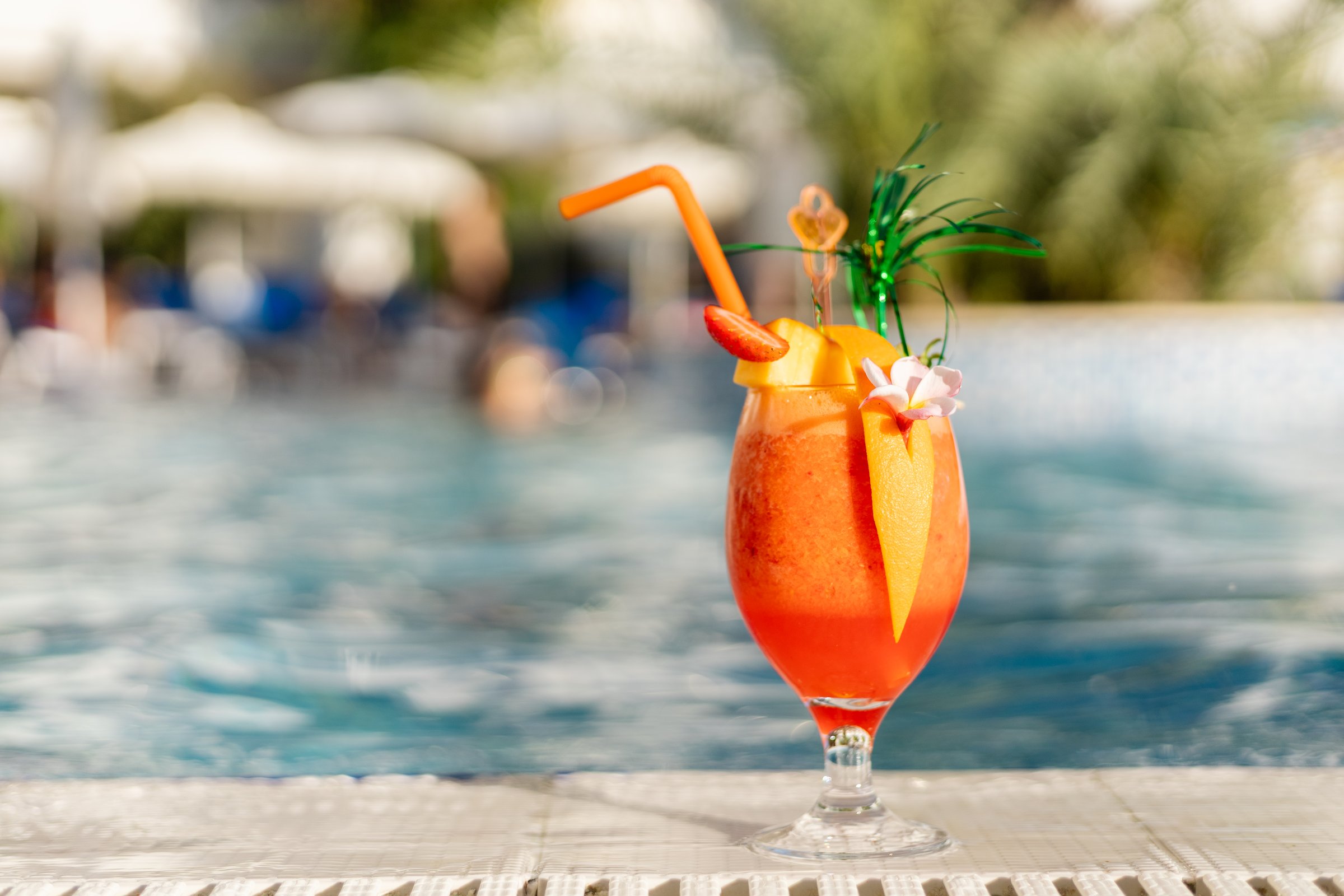 A drink with a colorful straw and decorations rests on the edge of a pool