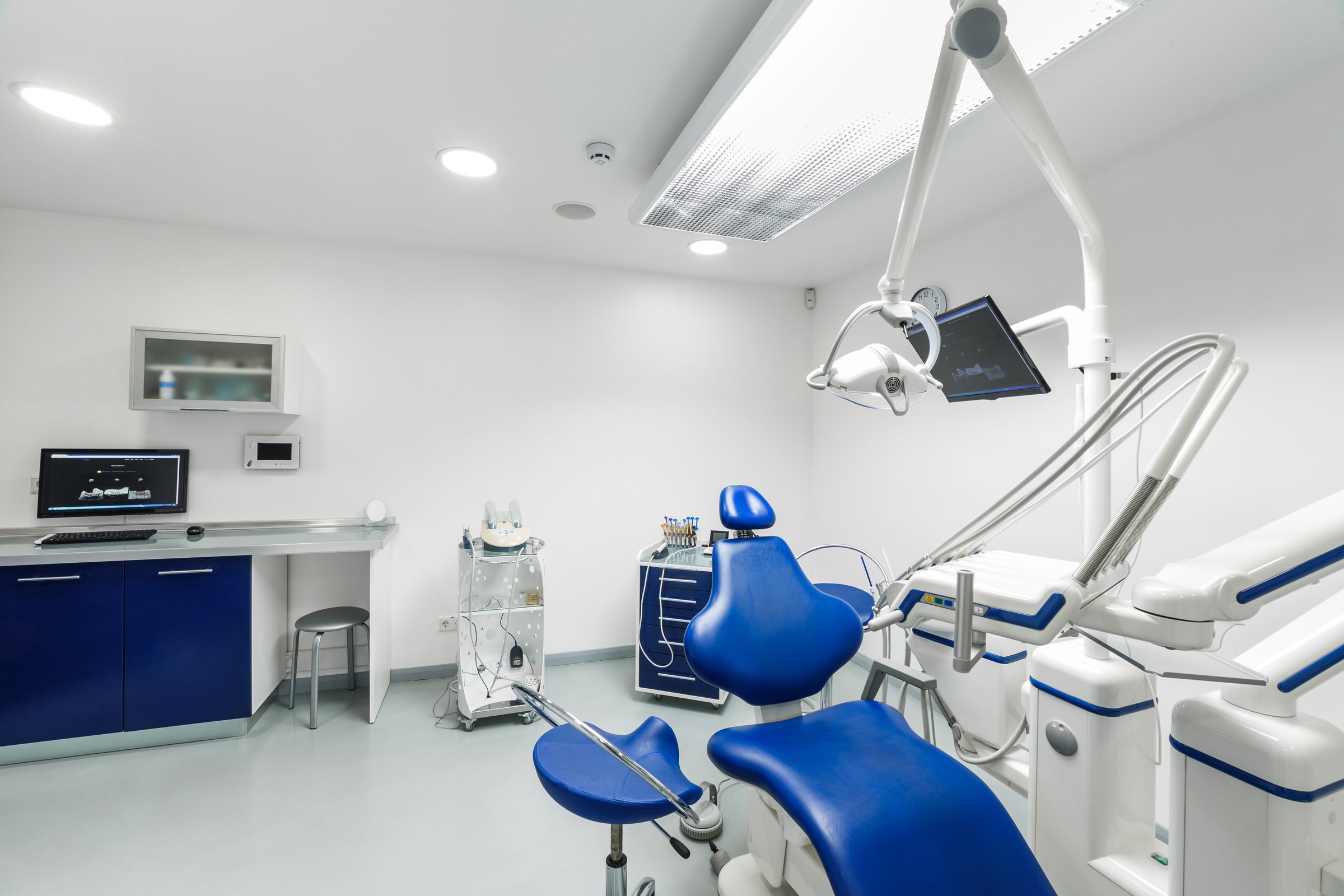 This image showcases a bright and modern dental clinic featuring a blue dental chair, advanced equipment, a patient monitor, and a clean, organized workspace for efficient dental treatments.