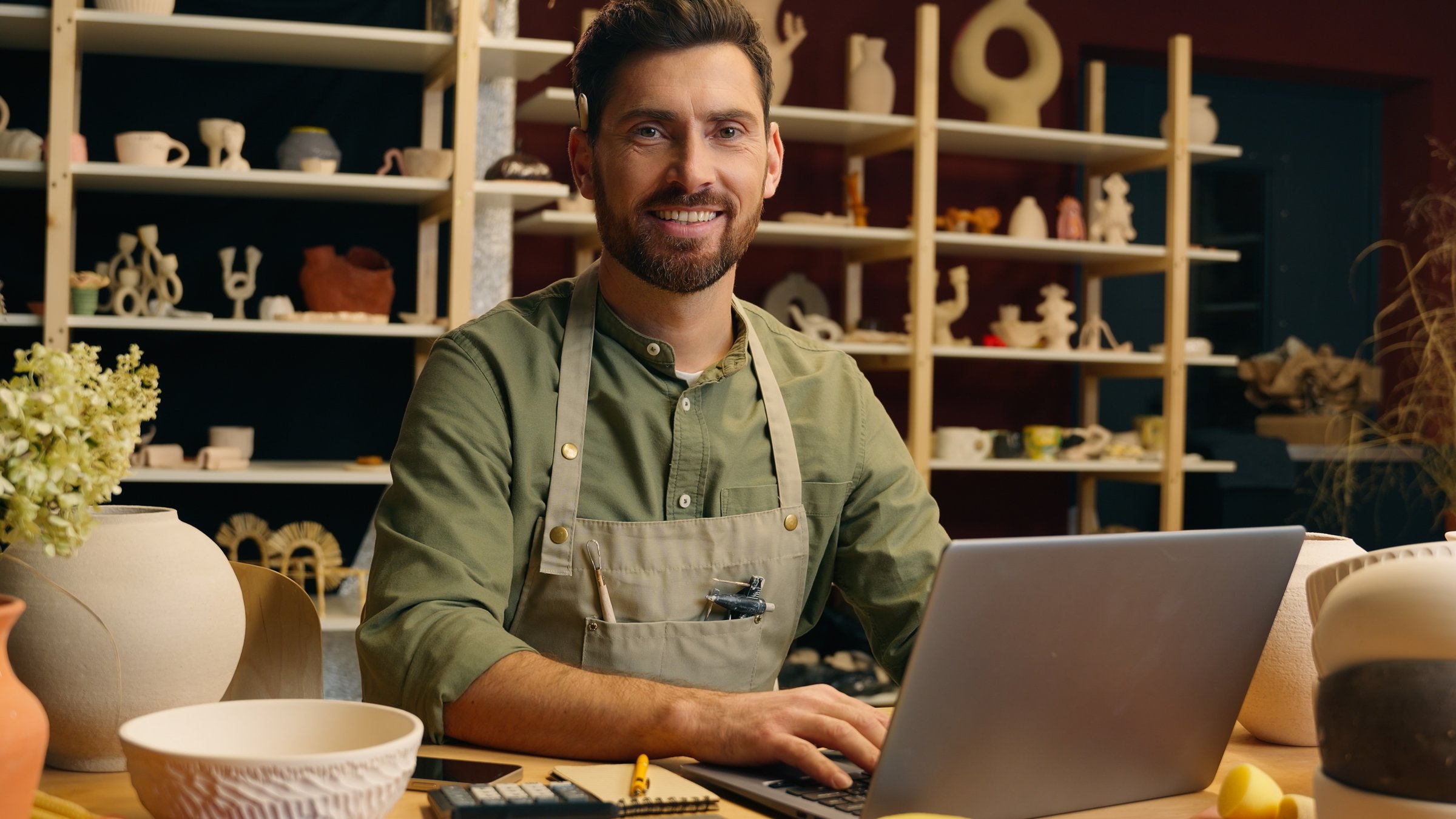 Happy smiling Caucasian man guy small business owner businessman successful entrepreneur crock potter artist male working computer typing laptop internet website looking camera inside pottery workshop. High quality 4k footage