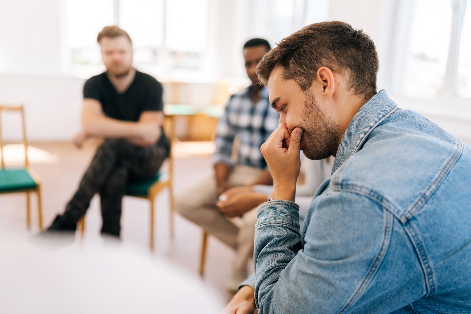 Closeup rear view of thoughtful young bearded man crying and talking about mental state sitting in circle during group therapy session. Concept of mental health, psychotherapy, social issues.