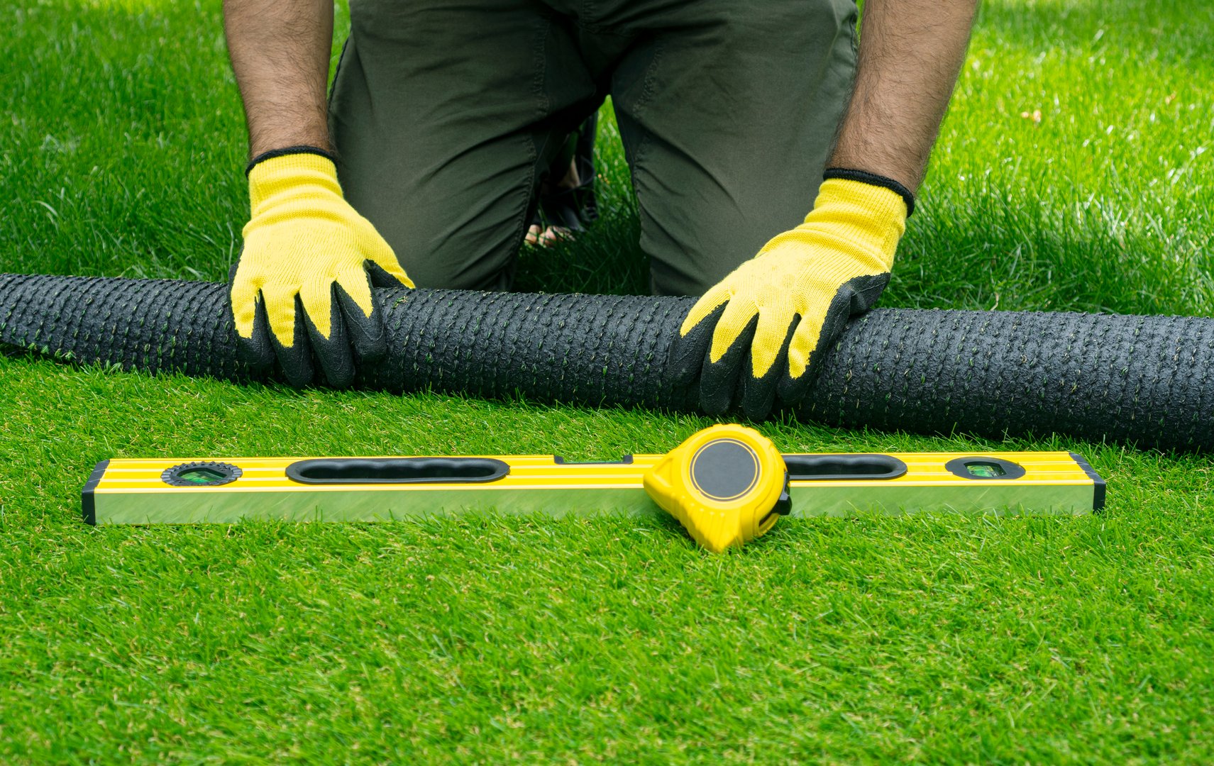 Landscaping of the yard with artificial turf. Male hands hold a roll of artificial grass.