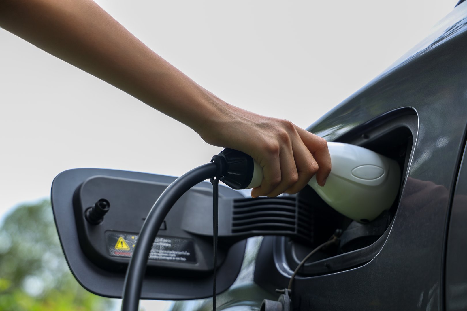 Woman hand puts the car on EV charging. Electric car Electric car charging in urban parking lot at day, Close Up