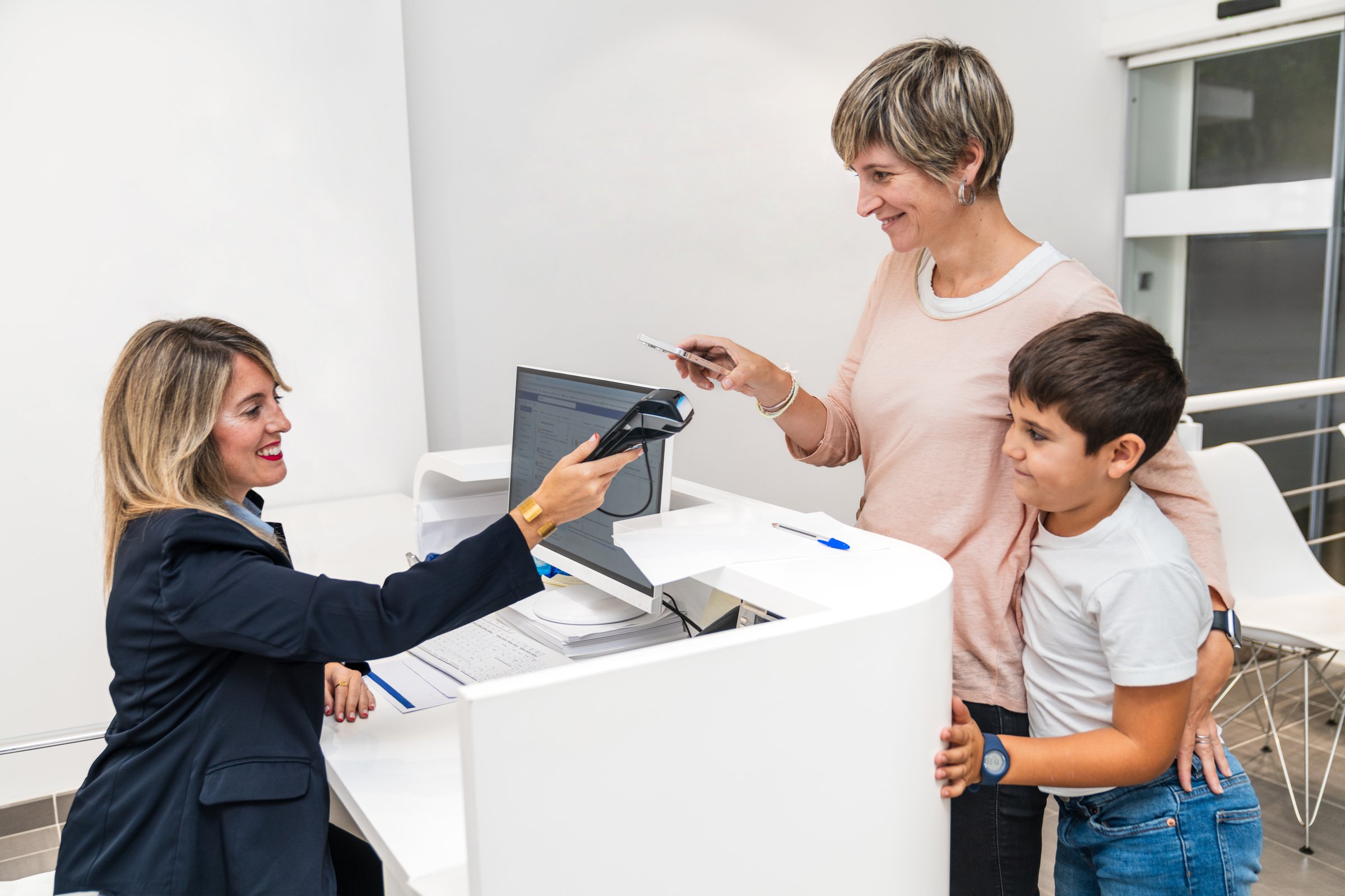A mother and her son are seen paying at a dental clinic's reception desk, interacting with the receptionist. Concept of payment and customer service.