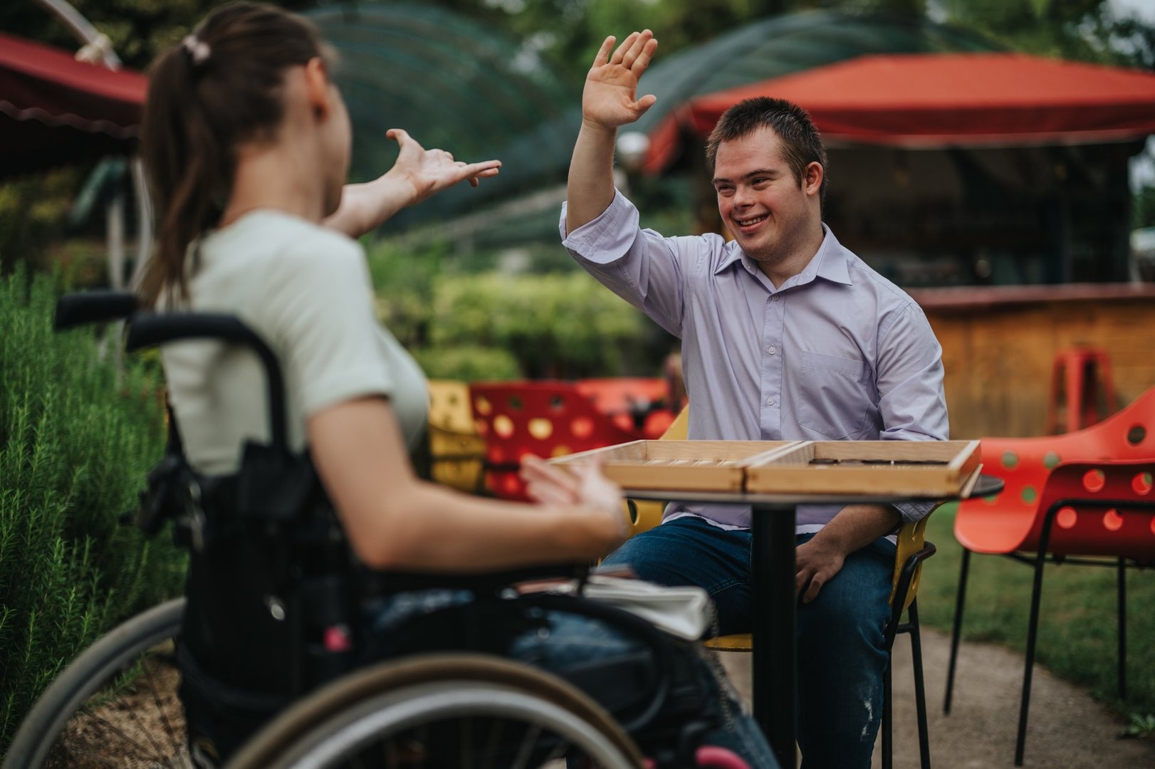 A boy with Down syndrome and a girl in a wheelchair share a lively, joyful moment in a vibrant outdoor setting, celebrating the value of friendship and inclusion.