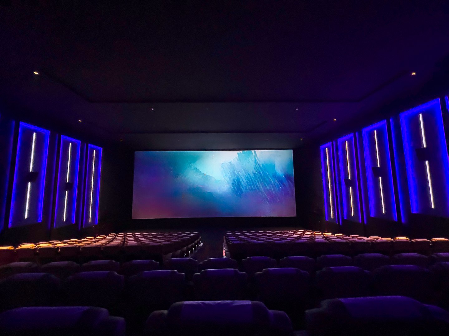 A pristine cinema hall with rows of plush, blue seats, a grand, illuminated screen, and subtle ambient lighting, creating an inviting atmosphere ready for the next audience.