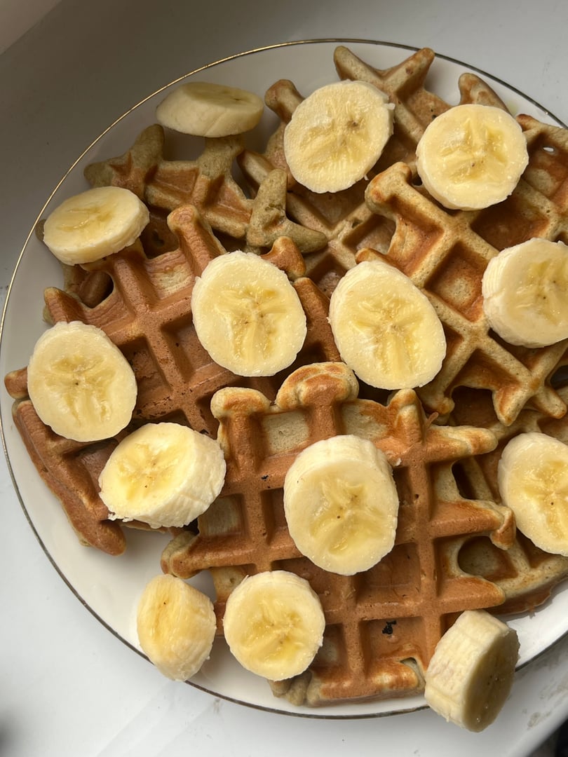 large plate on a white table with freshly bake round waffles with a banana healthy breakfast sweet