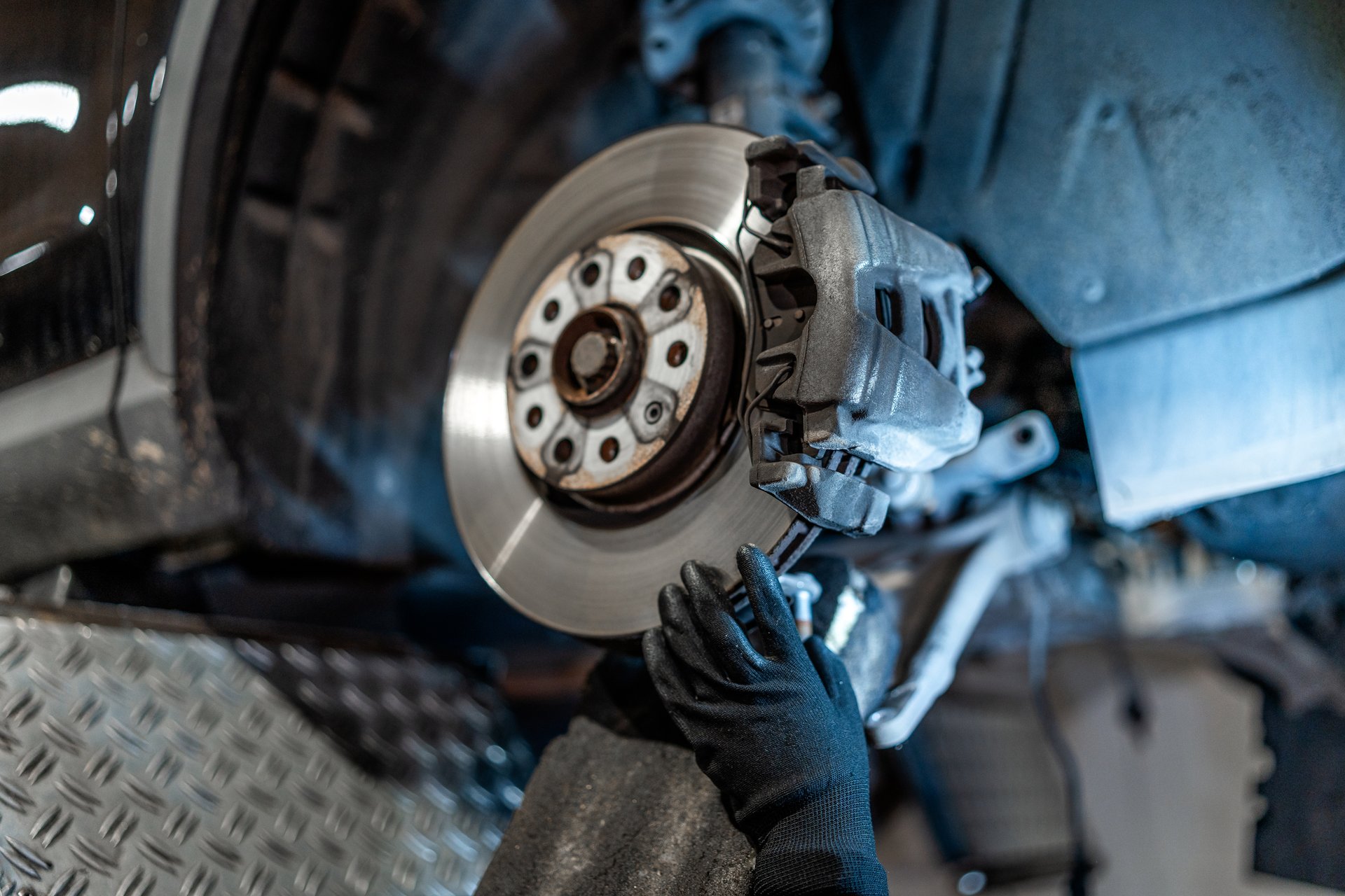 Close up of mechanic's hands wearing gloves, inspecting car brake disc and caliper during maintenance in auto repair shop